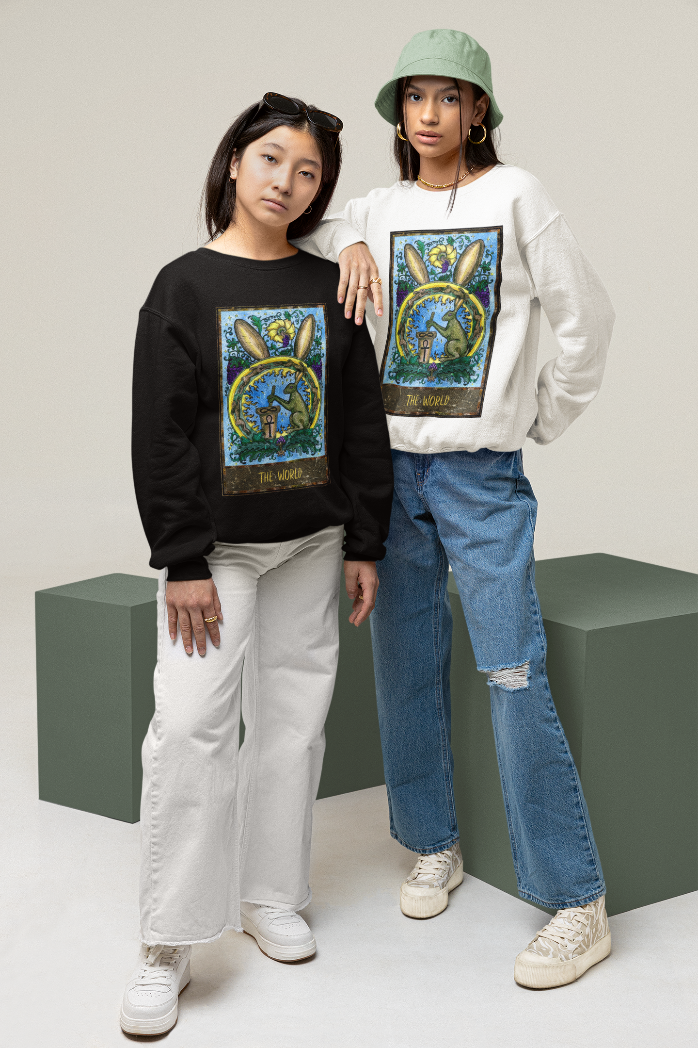 Two woman posing in a studio wearing a black and a white The World Tarot Card Sweatshirt