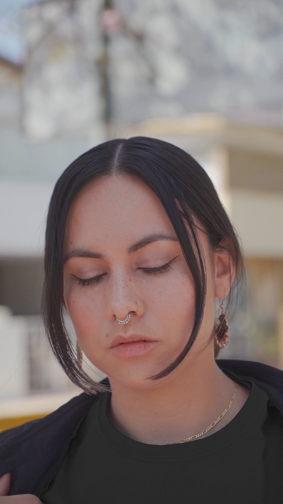 A video featuring woman wearing a black The High Priestess Tarot Card T-shirt, black long coat, and checkered pants posing in front of a cherry blossom tree