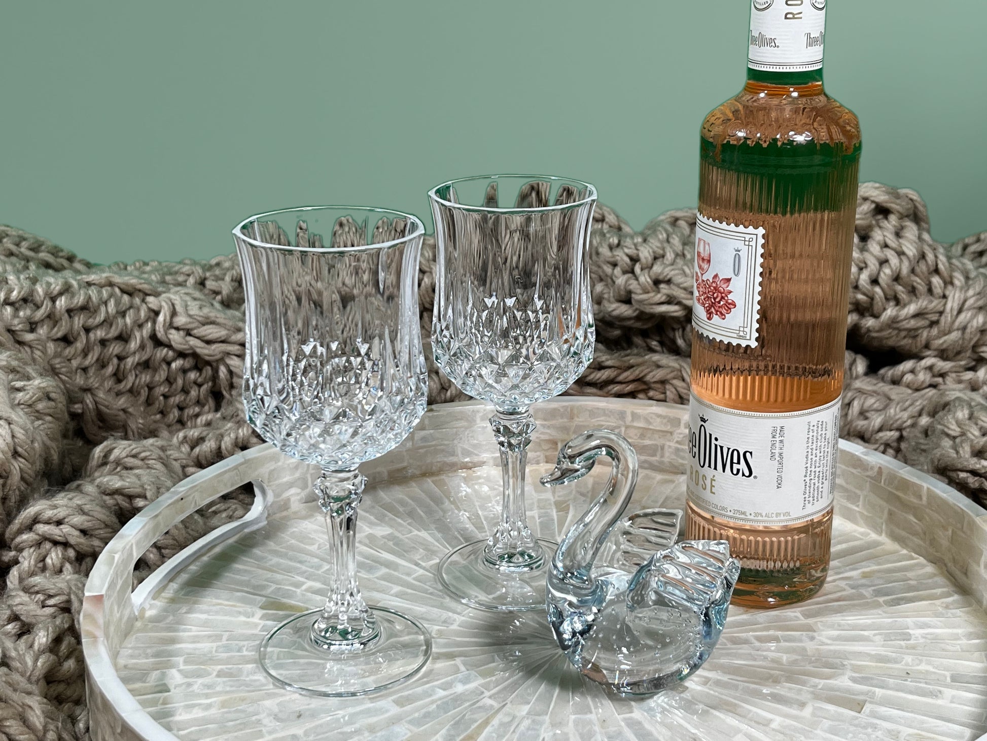 A close up shot of the South Sea White Mother of Pearl Tray on a khaki blanket, with glasses, a bottle, and a glass swan