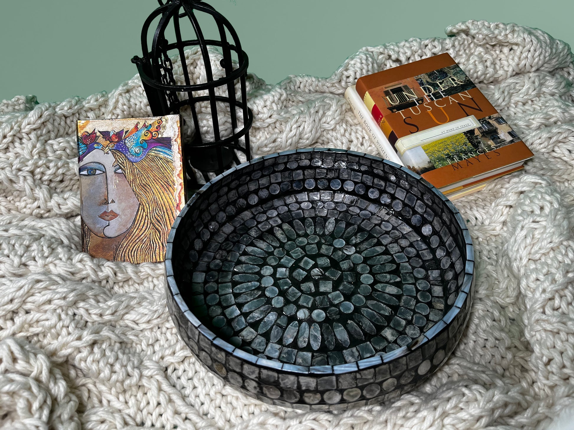 a top shot of the Curvy Round Mother of Pearl Tray on a blanket, with books and decoration in the back