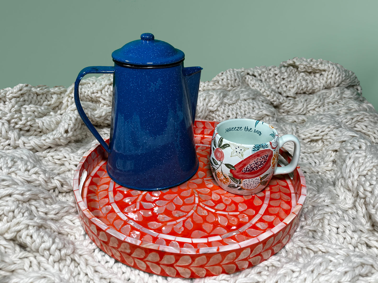 A Deep Coral Mother of Pearl Tray on a beige blanket that has blue water kettle and a fruit pattern cup 