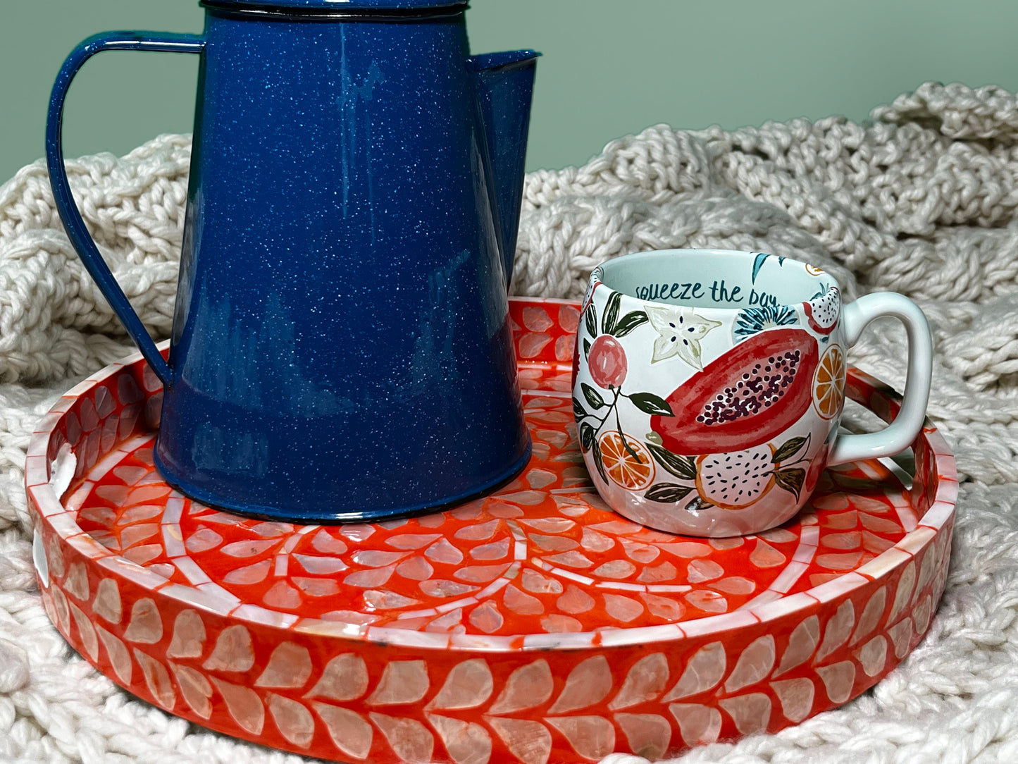 close up shot of A Deep Coral Mother of Pearl Tray on a beige blanket that has blue water kettle and a fruit pattern cup 