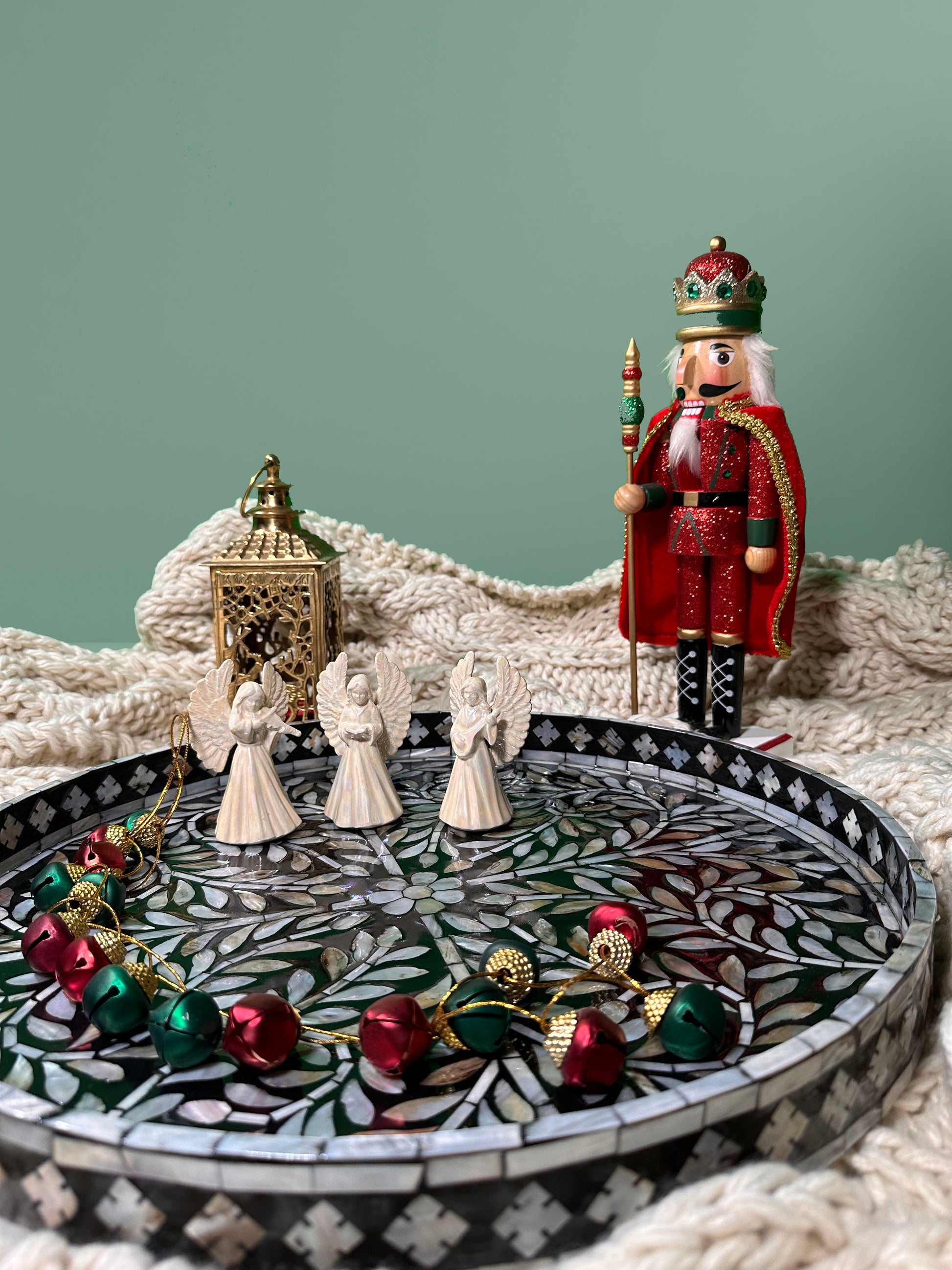 The large Black Sea Mother of Pearl Tray on a blanket, a gold candle holder, a Christmas nut cracker, Christmas bells, and three angels