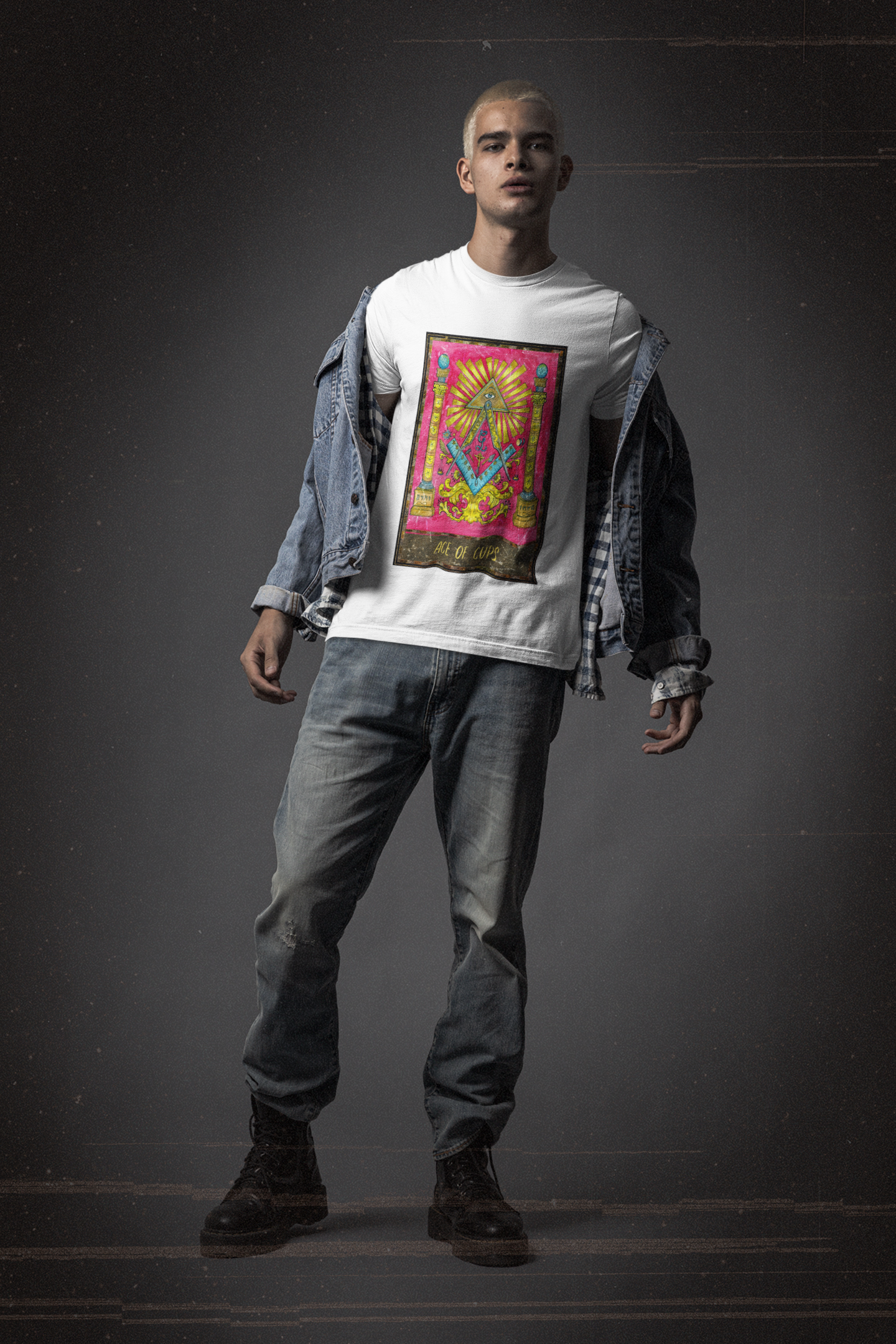 White man wearing a white ace of cups tarot card t-shirt, a bluish gray denim jacket, blue denim jeans, and black pair of boots posing in a black background studio