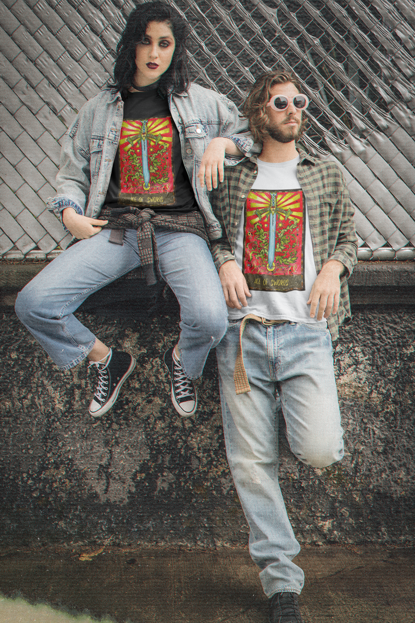 A couple posing in front of a wall: the woman is wearing a black Ace of Swords Tarot Card T-shirt, blue denim jacket, blue jeans, and black and white shoes; the man is wearing sunglasses, a white Ace of Swords Tarot Card T-shirt, striped collar shirt, blue jeans. and black shoes