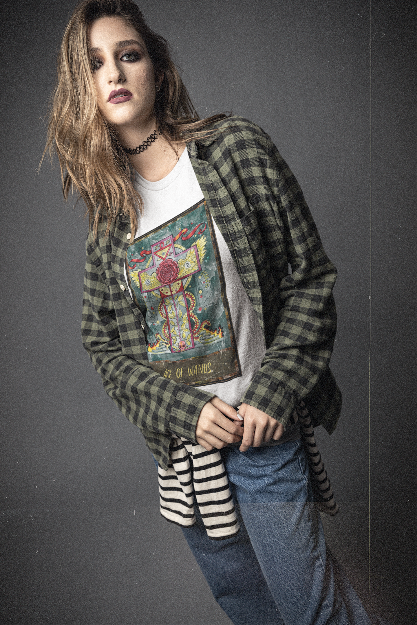 A woman wearing a white Ace of Wands Tarot Card T-shirt, black and green checkered shirt, blue jeans, and a black and white striped shirt tying around her waist