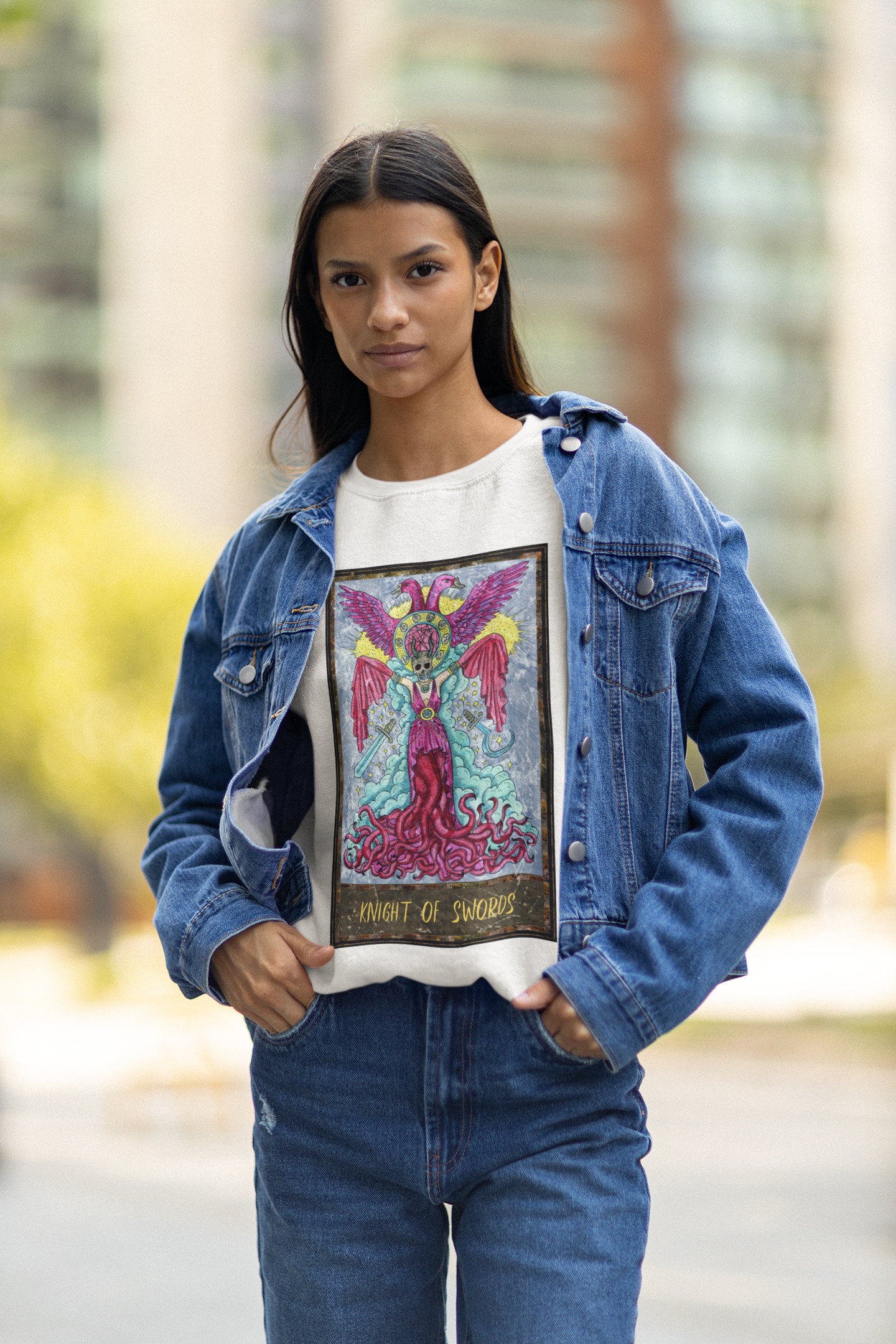 A woman posing wearing a white Knight of Swords Tarot Card Sweatshirt, a denim jacket and blue jeans