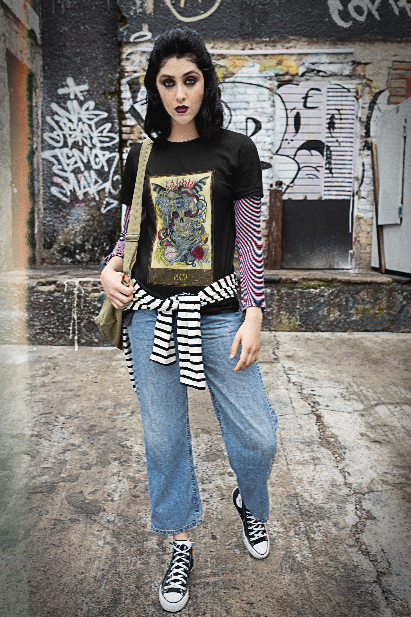 A woman wearing a black Death Tarot Card T-Shirt over a patterned shirt, blue jeans with a black and white stripe shirt trying around her waist, and black and white shoes