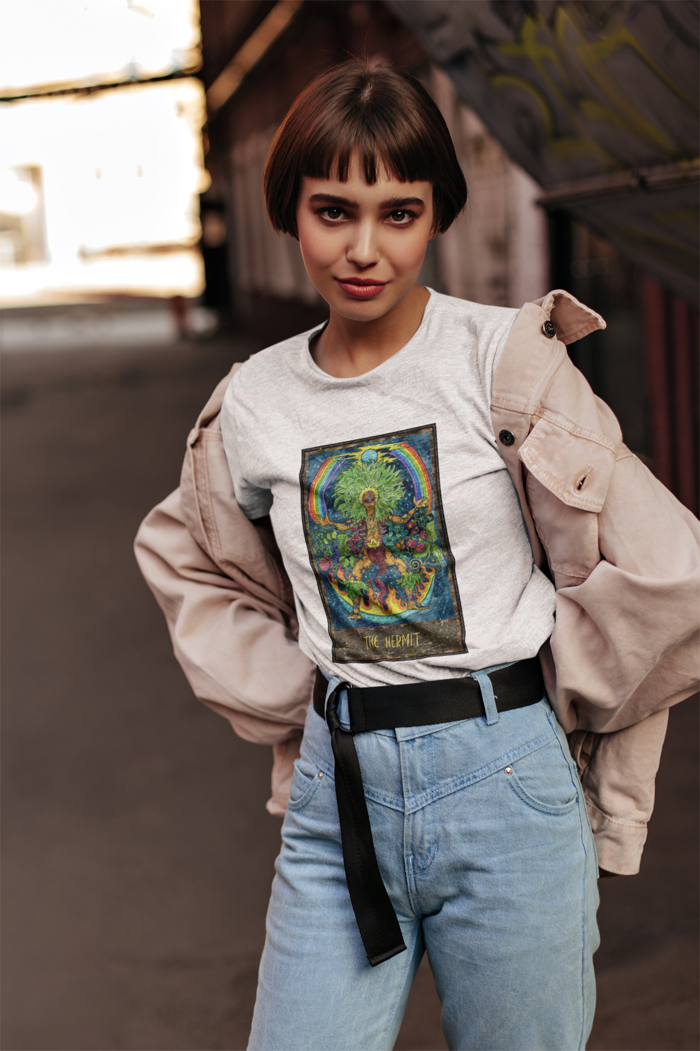 A woman with short hair wearing a white The Hermit Tarot Card T-shirt, pink jacket and blue jeans