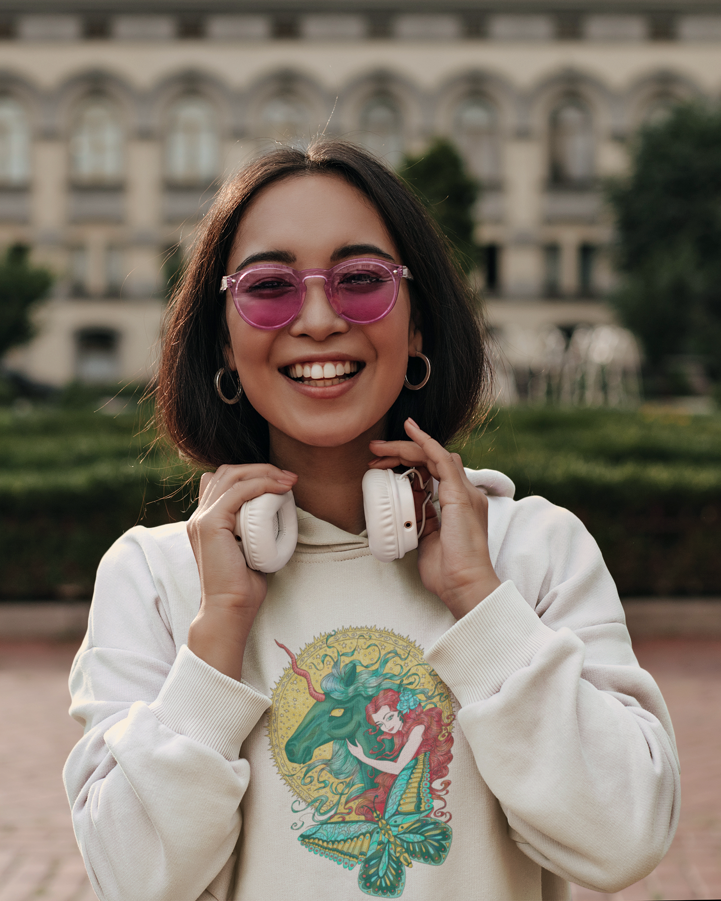 A happy woman with headphone and pink sunglasses wearing a white Poppy Red Princess and Magic Unicorn Hoodie