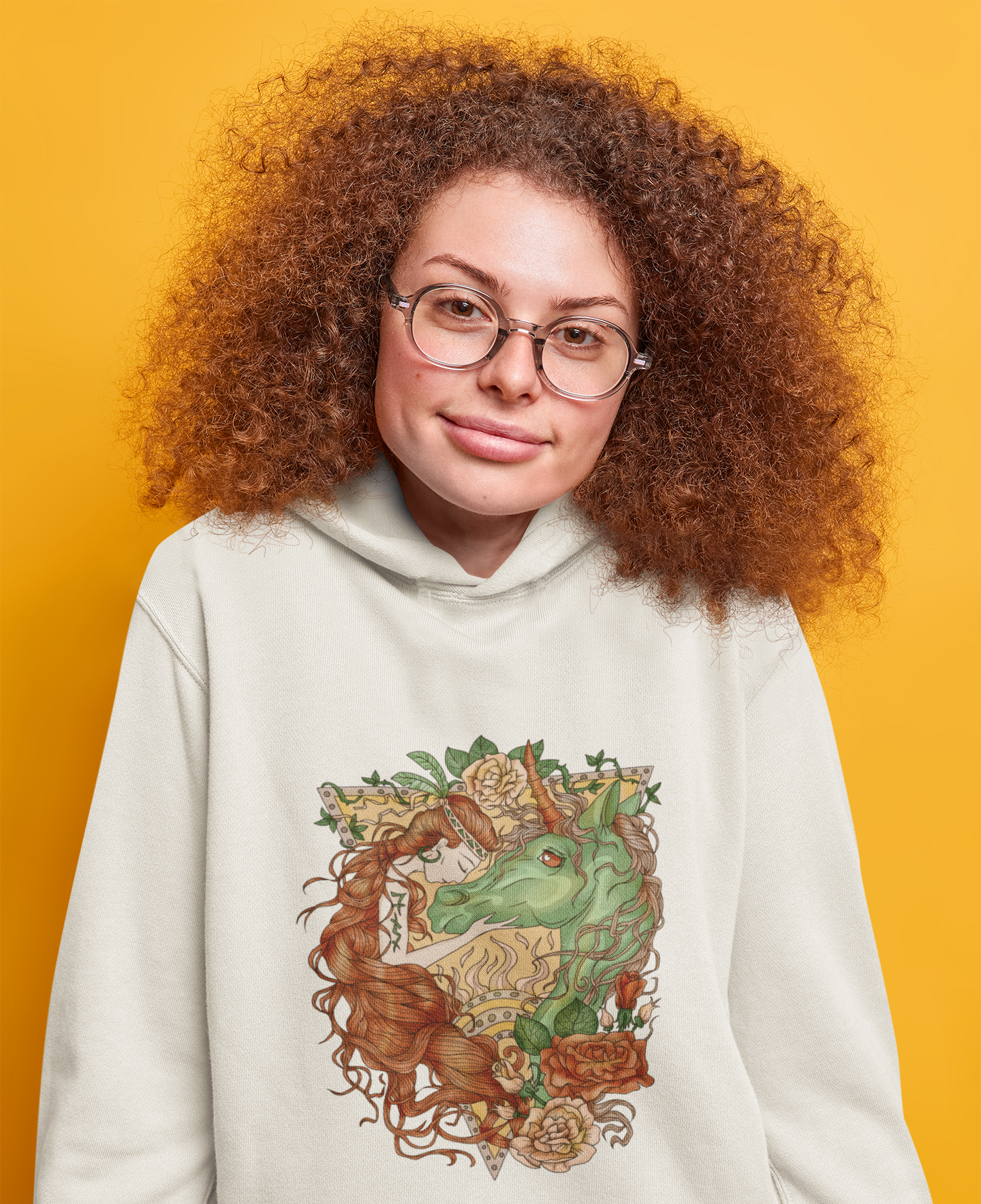 A curly haired woman with glasses in a studio with orange background, wearing a white Cocoa Brown Princess and Magic Unicorn Hoodie