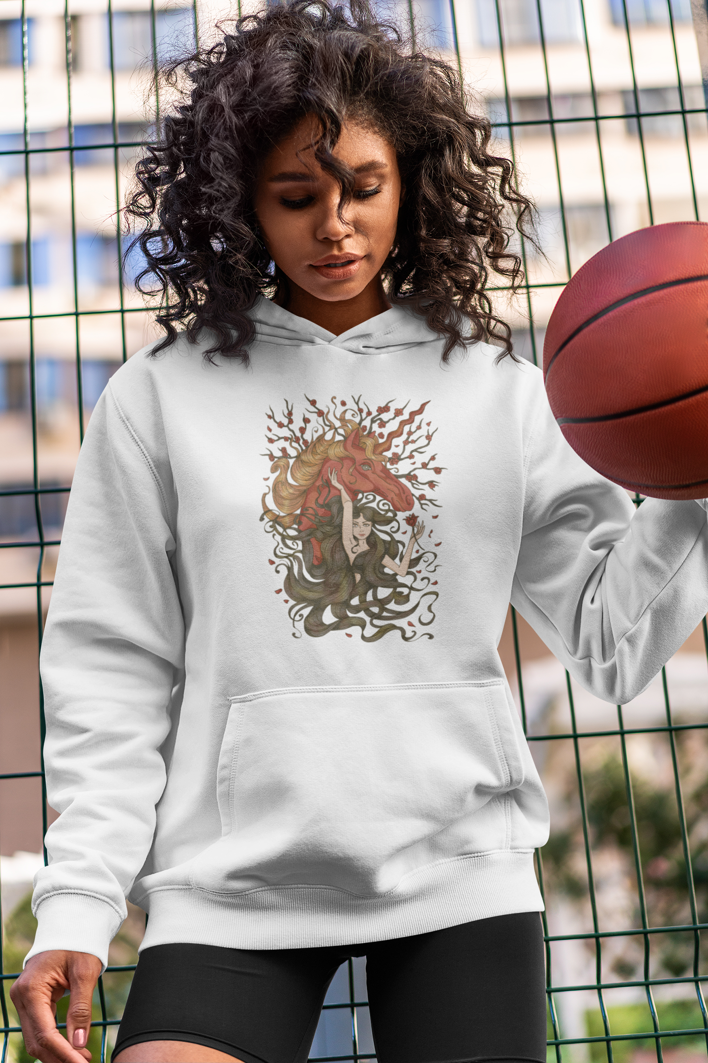 A woman wearing a white Walnut Brown Princess and Magic Unicorn Hoodie with black shorts dribbling a basketball