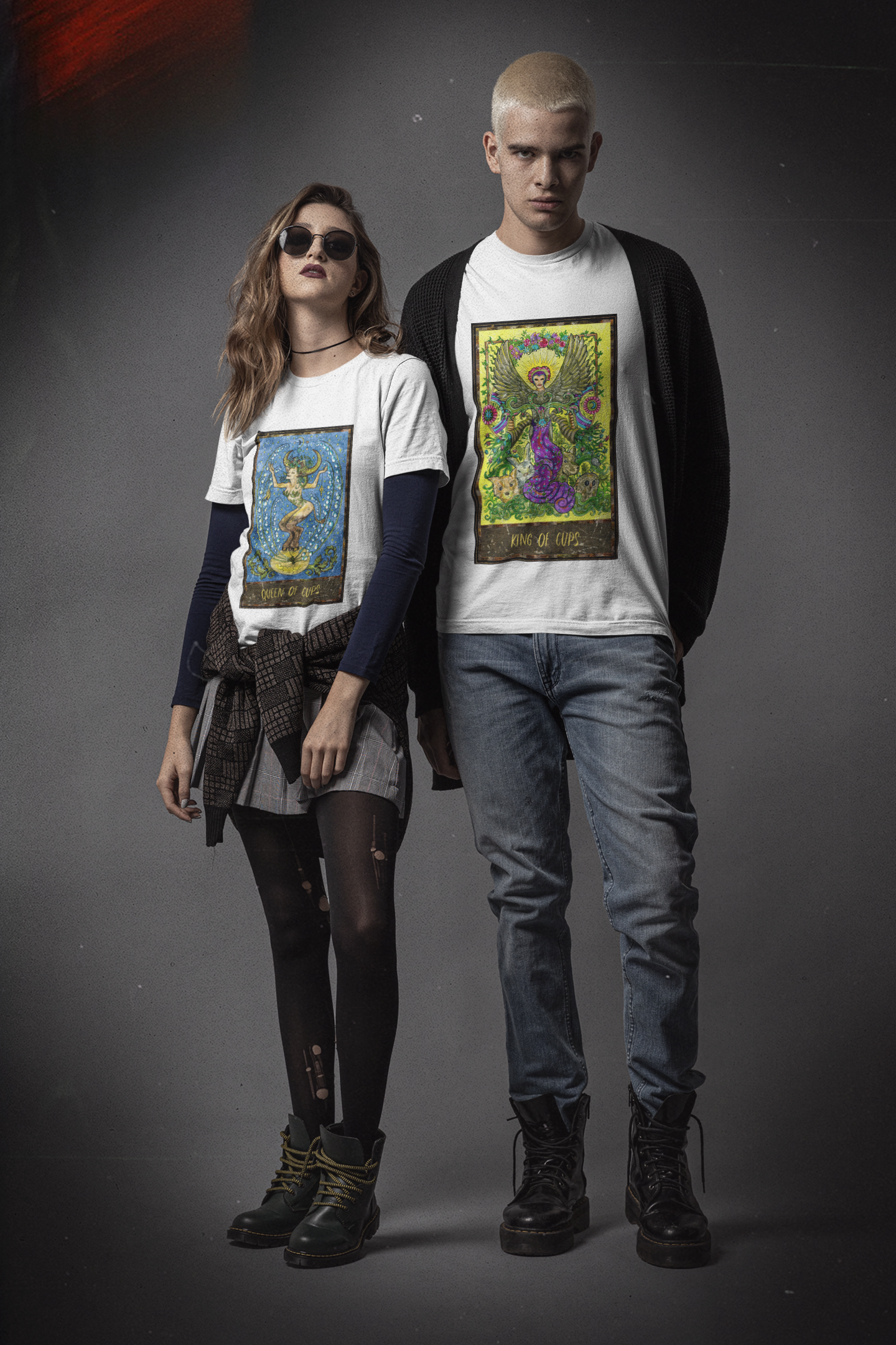 A woman wearing a white Queen of Cups Tarot Card T-Shirt, grey skirt with ripped black stockings, and black boots. A man wearing a white King of Cups Tarot Card T-Shirt, black cardigan, jeans, and black boots