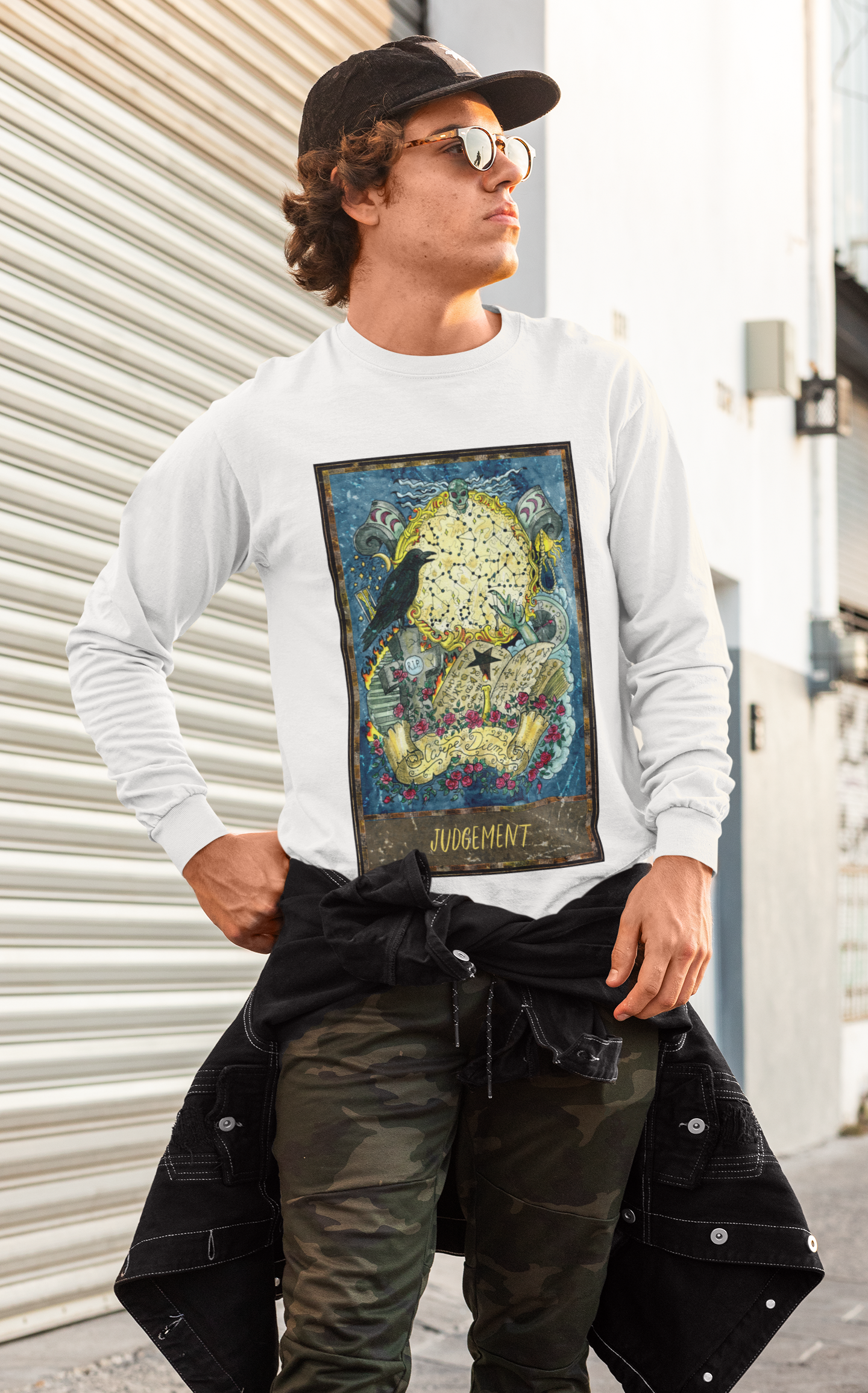 A man with sunglasses and a cap posing with a white Judgement - Tarot Card Sweatshirt, camo pants and a black shirt tying around his waist