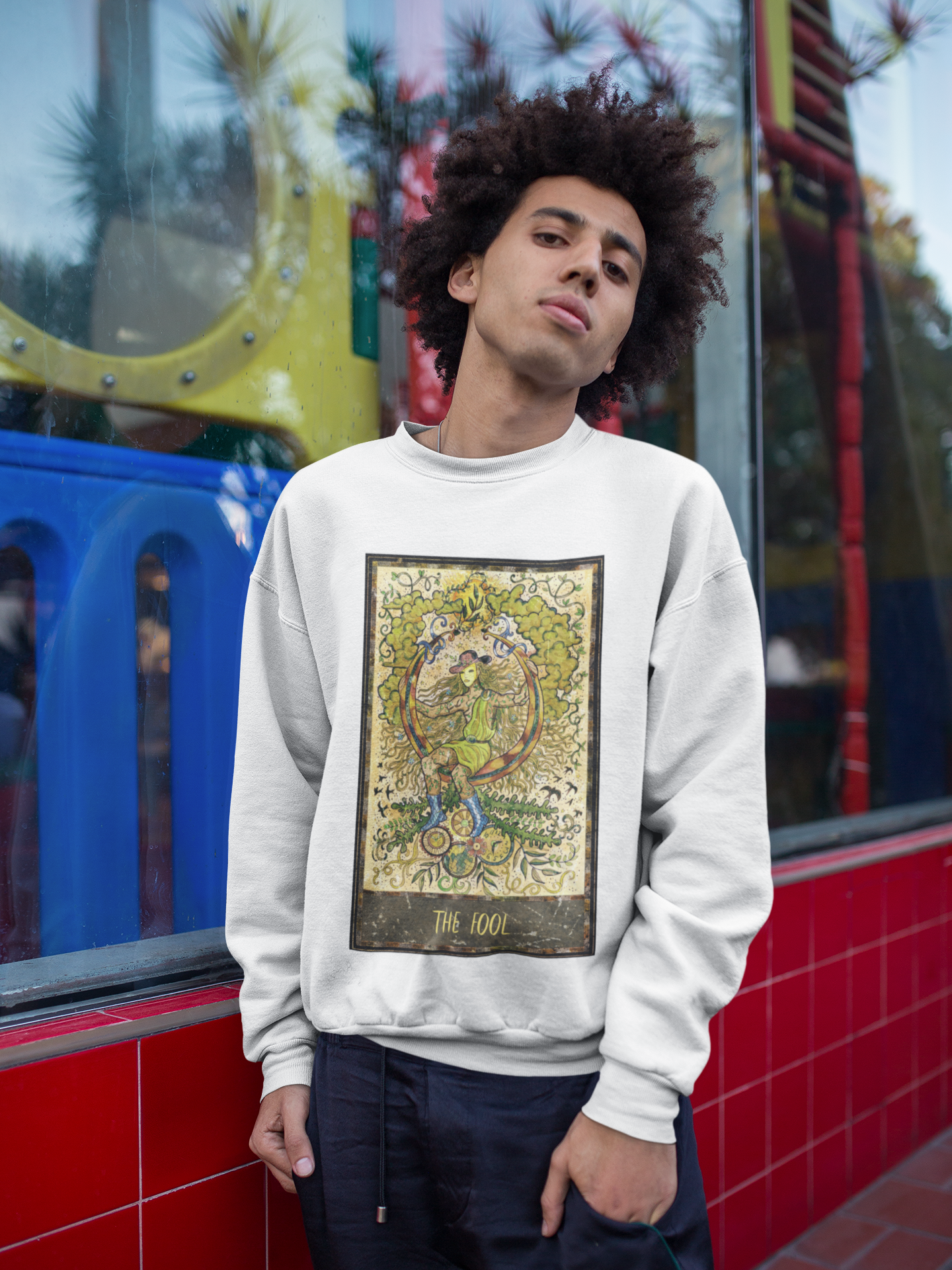 A man wearing a white The Fool Tarot Card Sweatshirt with black pants