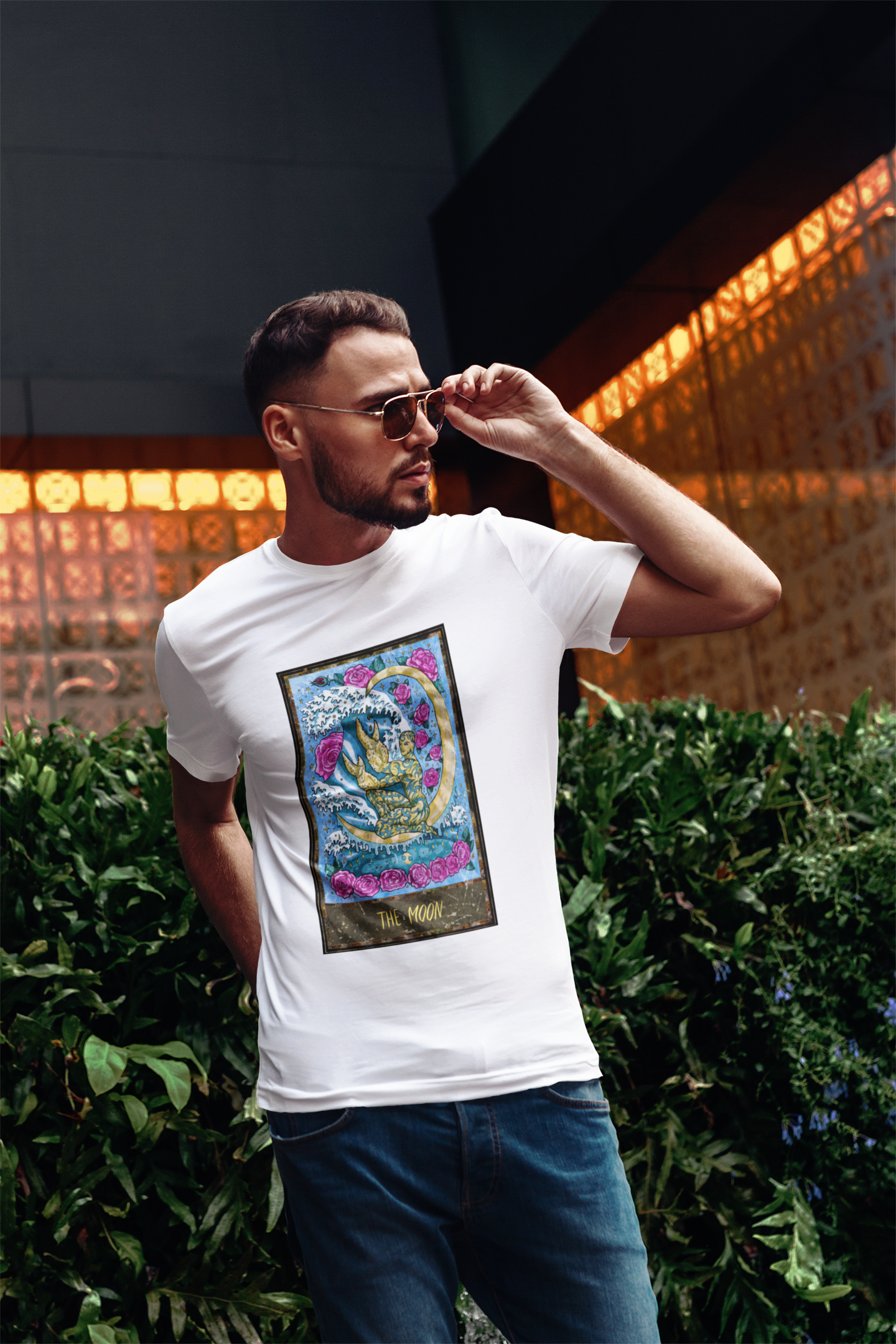 A man with stylish sunglasses wearing a white The Moon Tarot Card T-shirt and jeans