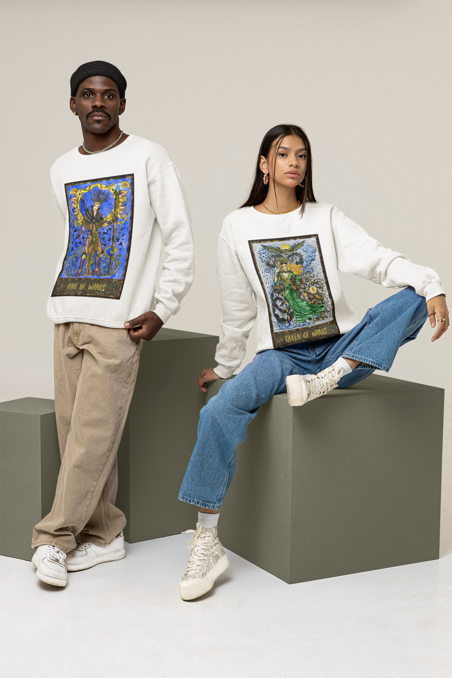 A woman wearing a white Queen of Wands Tarot Card Sweatshirt, blue jeans, and white shoes. A man wearing a white King of Wands Tarot Card Sweatshirt, beige pants and white shoes