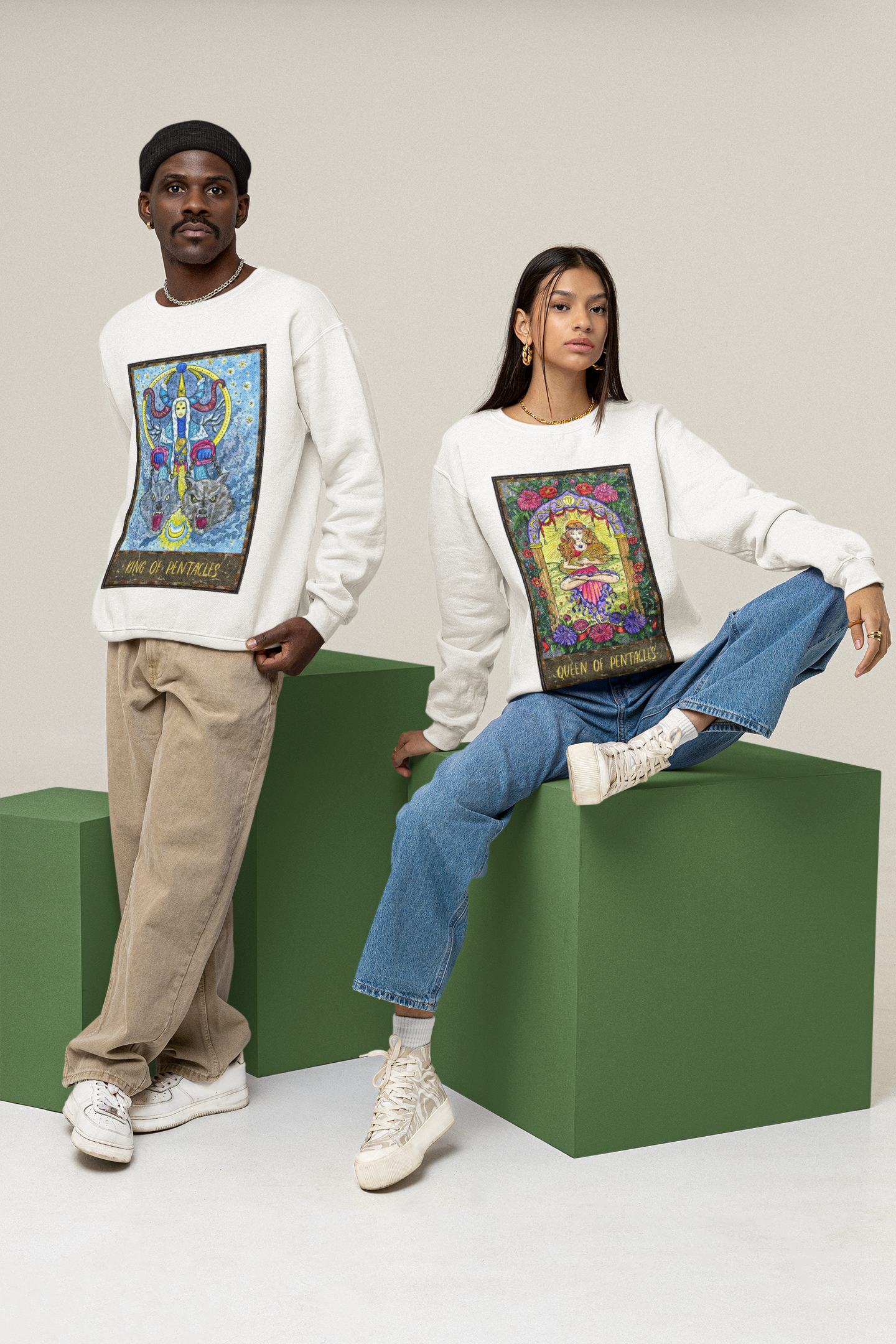 A woman wearing a white Queen of Pentacles Tarot Card Sweatshirt, blue jeans with white shoes. A man wearing a white King of Pentacles Tarot Card Sweatshirt, beige pants, white shoes