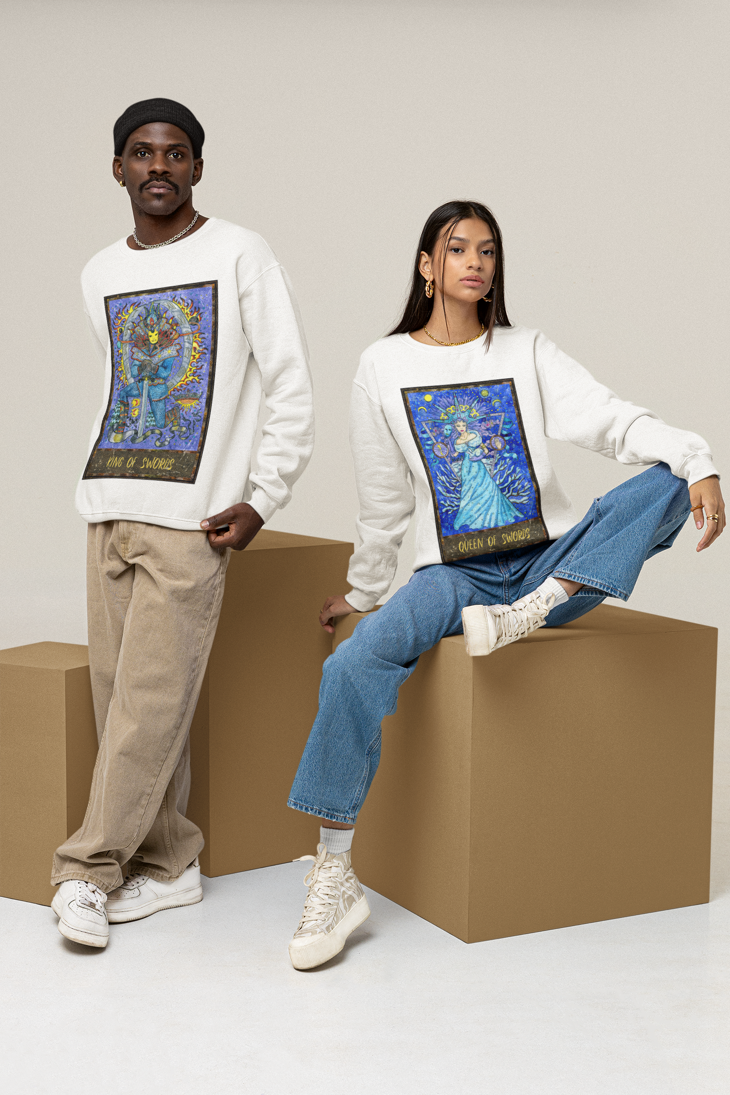 A man wearing a white King of Swords Tarot Card Sweatshirt, beige pants, and white shoes. A woman wearing a white Queen of Swords Tarot Card Sweatshirt, blue jeans, and white shoes