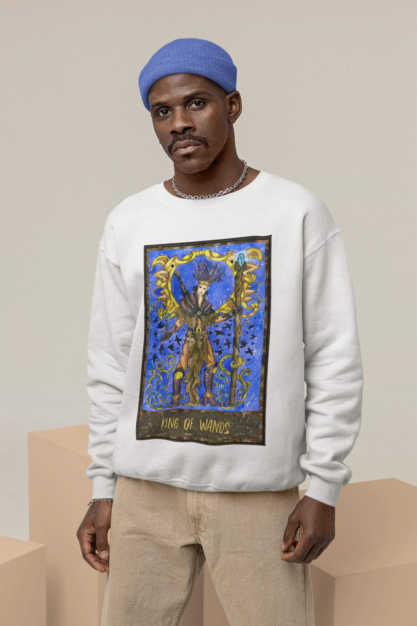 A man with a blue beanie wearing a white King of Wands Tarot Card Sweatshirt, and beige pants