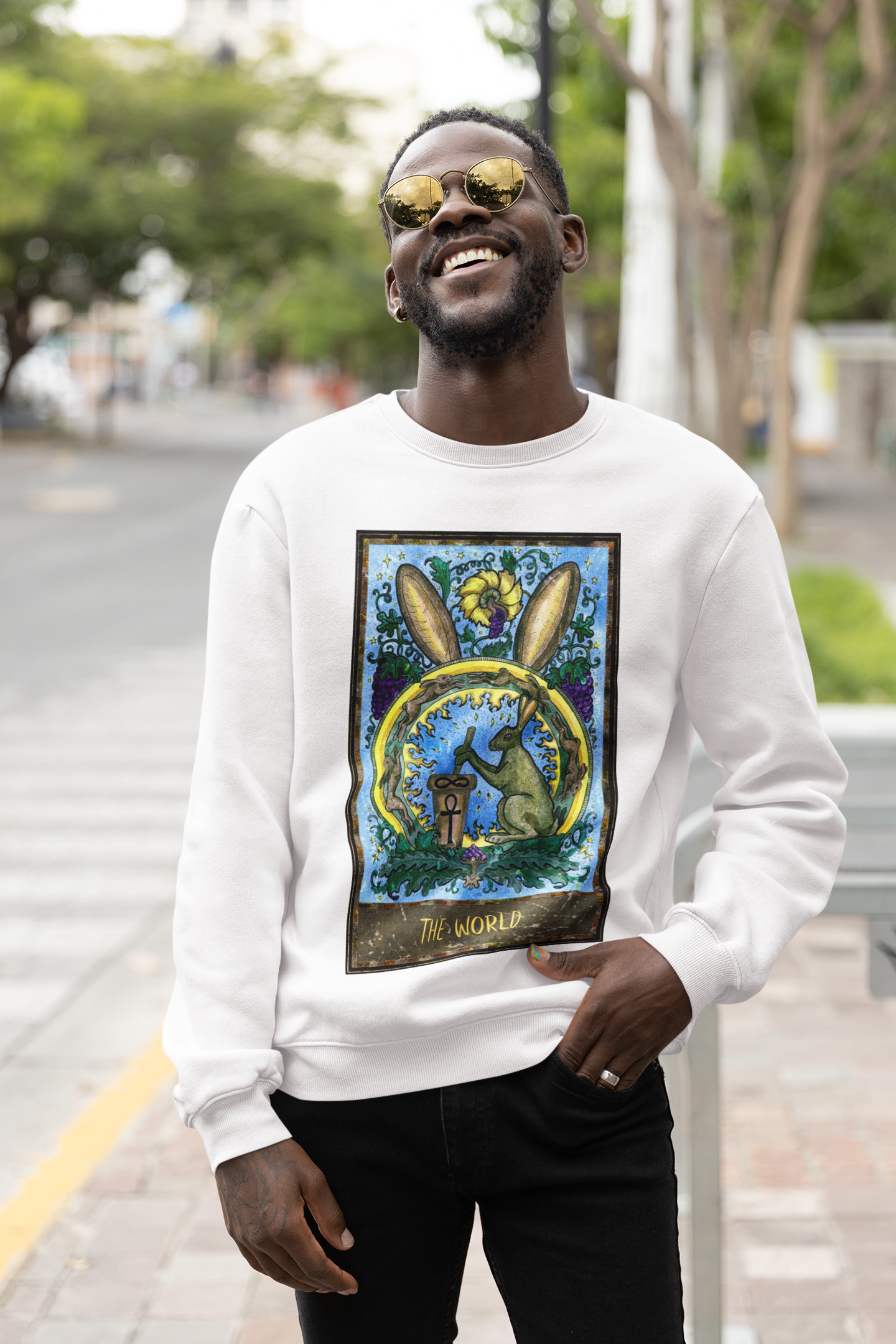 A man with sunglasses wearing a white The World Tarot Card Sweatshirt and black pants 