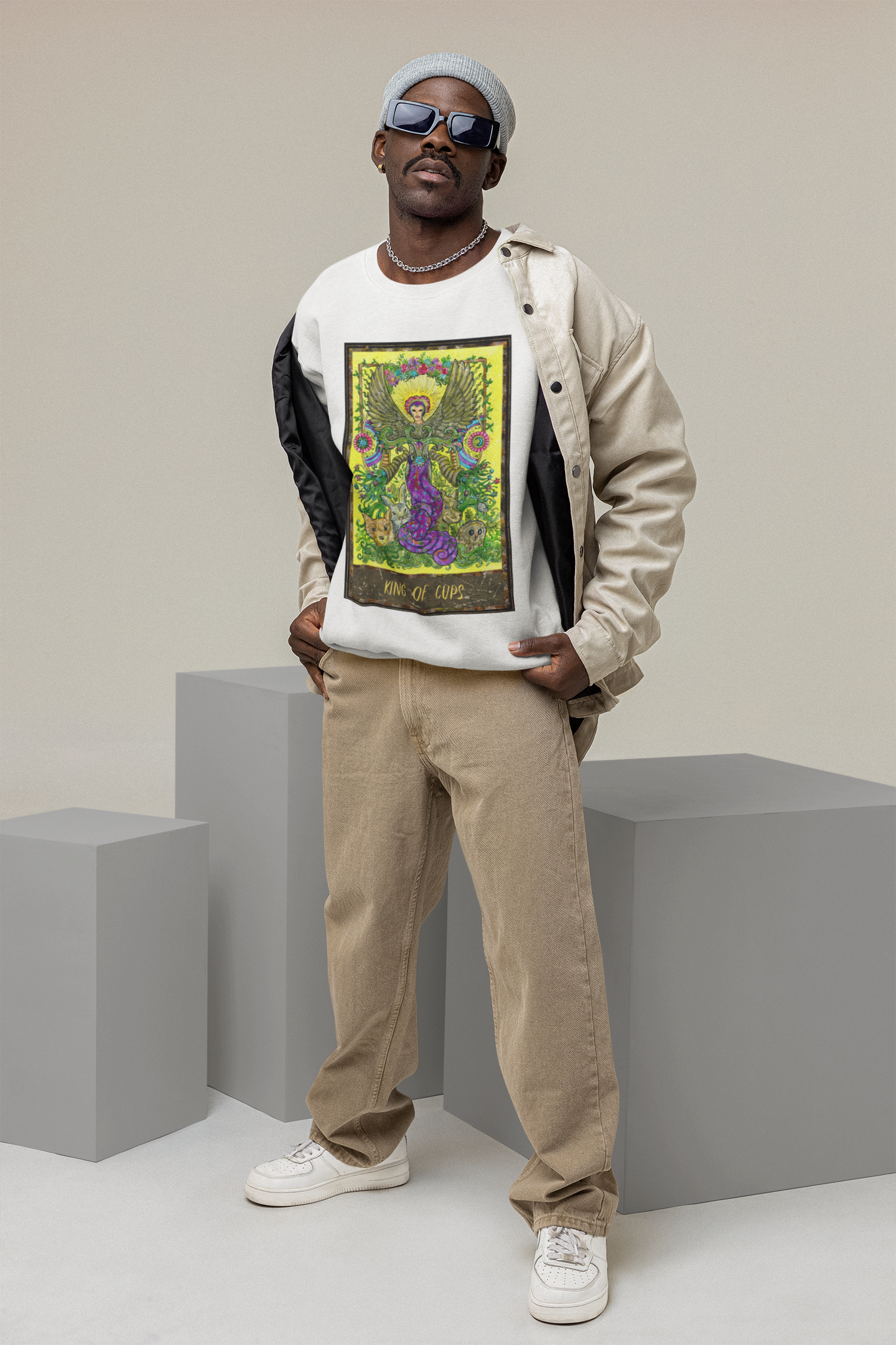 A stylish man wearing a King of Cups Tarot Card Sweatshirt a beige jacket, jeans, and white shoes