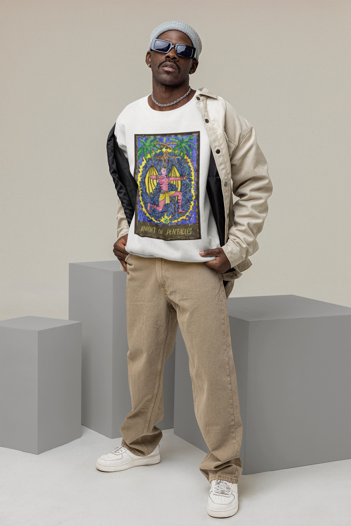 A man in sunglasses wearing a white Knight of Pentacles Tarot Card Sweatshirt, beige jacket and pants, and white shoes