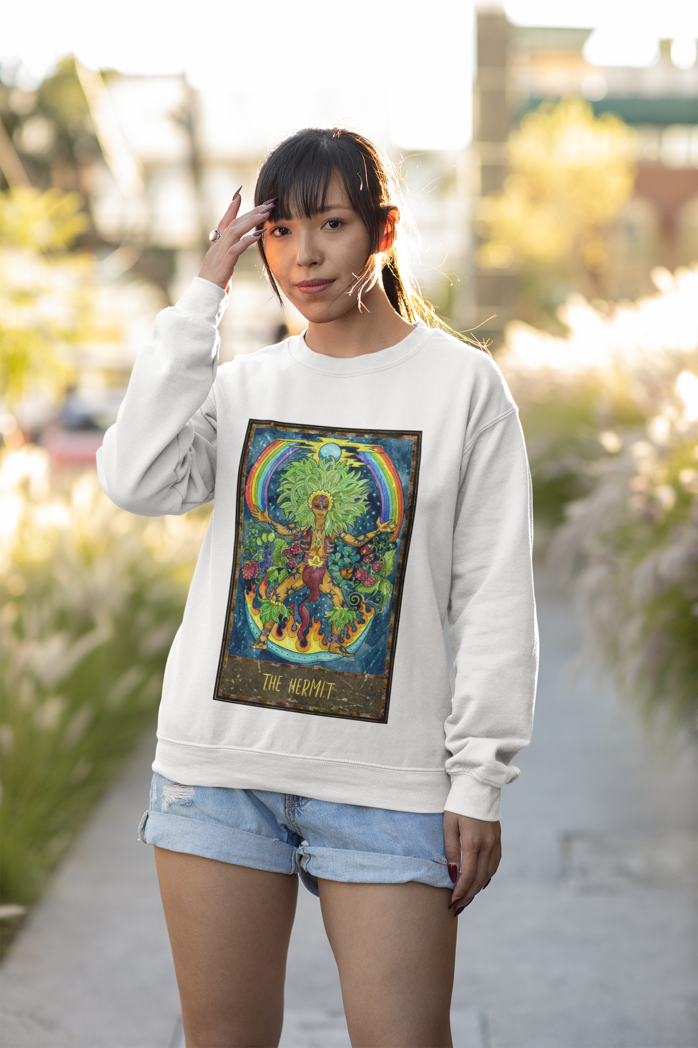 A woman wearing a white The Hermit Tarot Card Sweatshirt and denim shorts