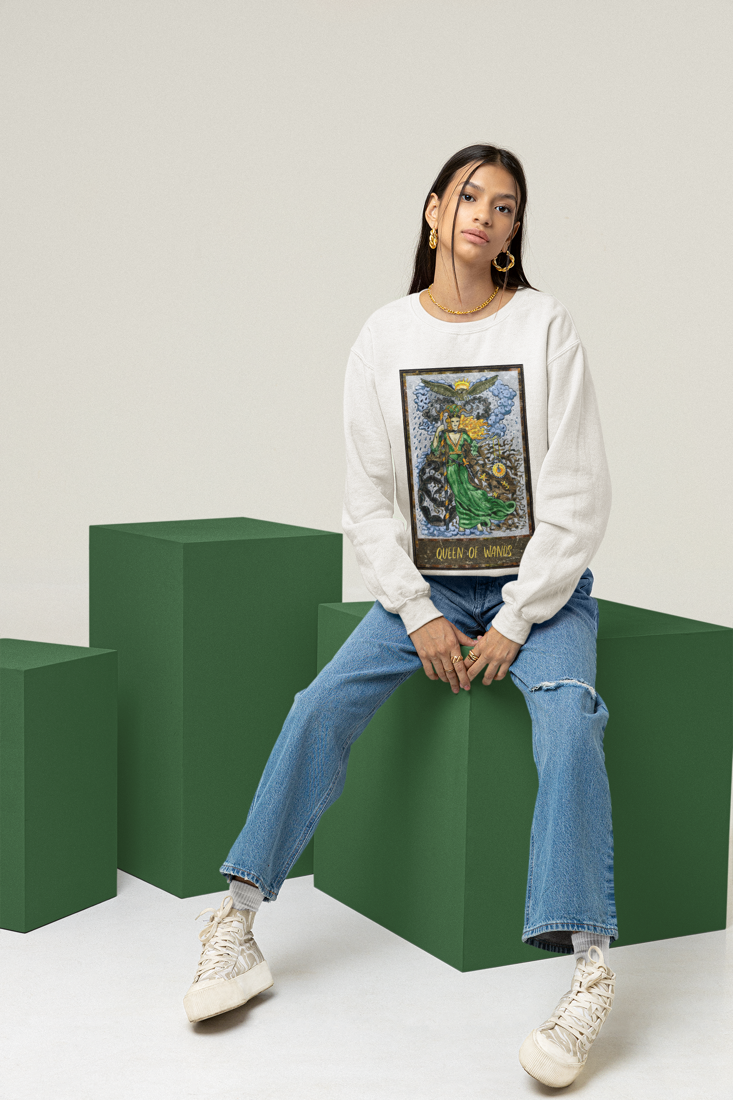 A woman wearing a white Queen of Wands Tarot Card Sweatshirt, blue jeans, and white shoes