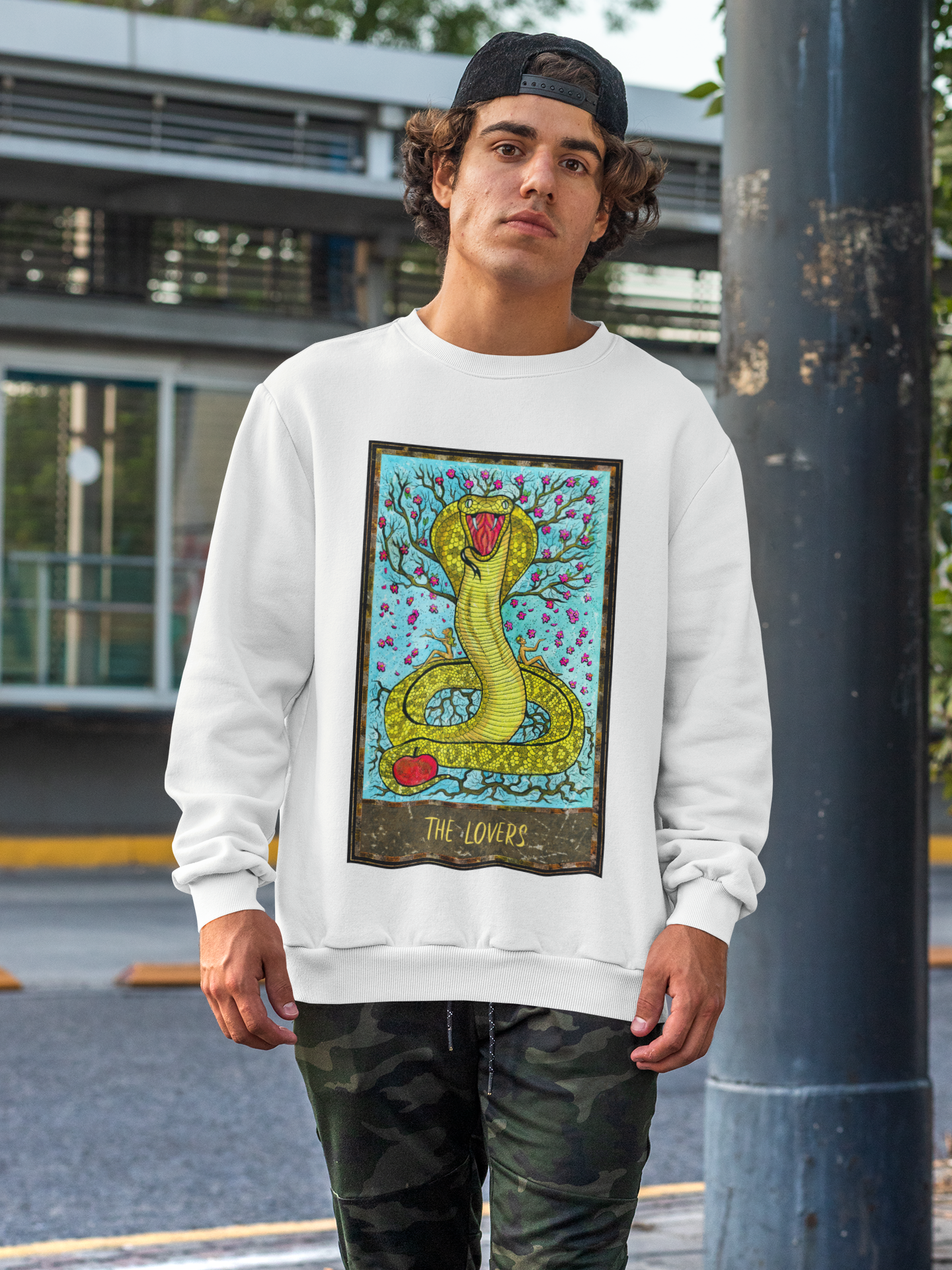 A man wearing a white The Lovers Tarot Card Sweatshirt and camo pants