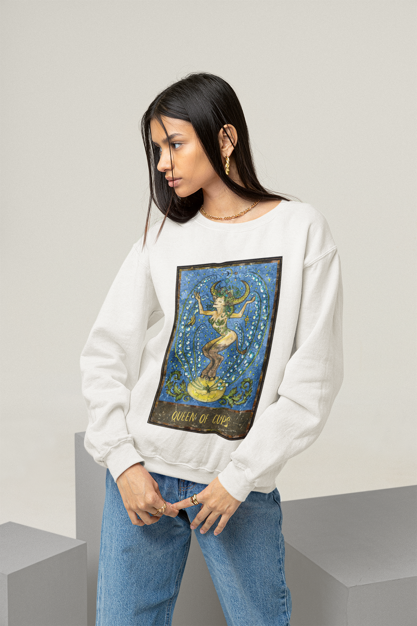 A young woman wearing a white Queen of Cups Tarot Card Sweatshirt and blue jeans