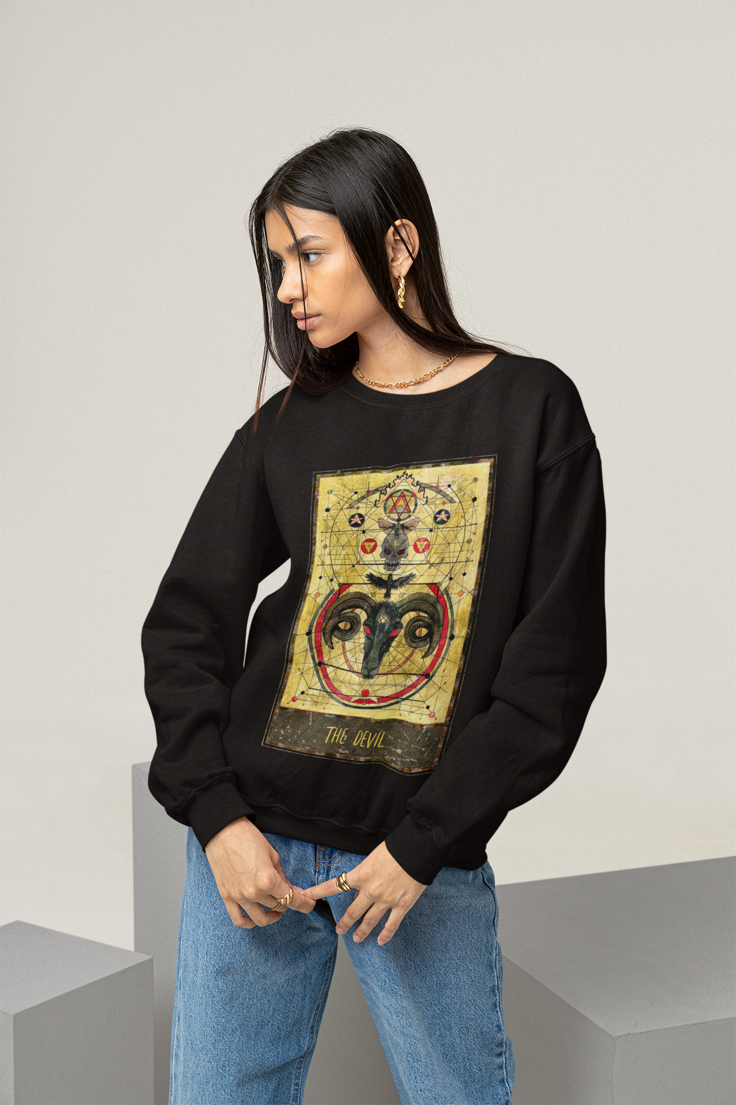 A young woman wearing a black The Devil Tarot Card Sweatshirt and blue jeans