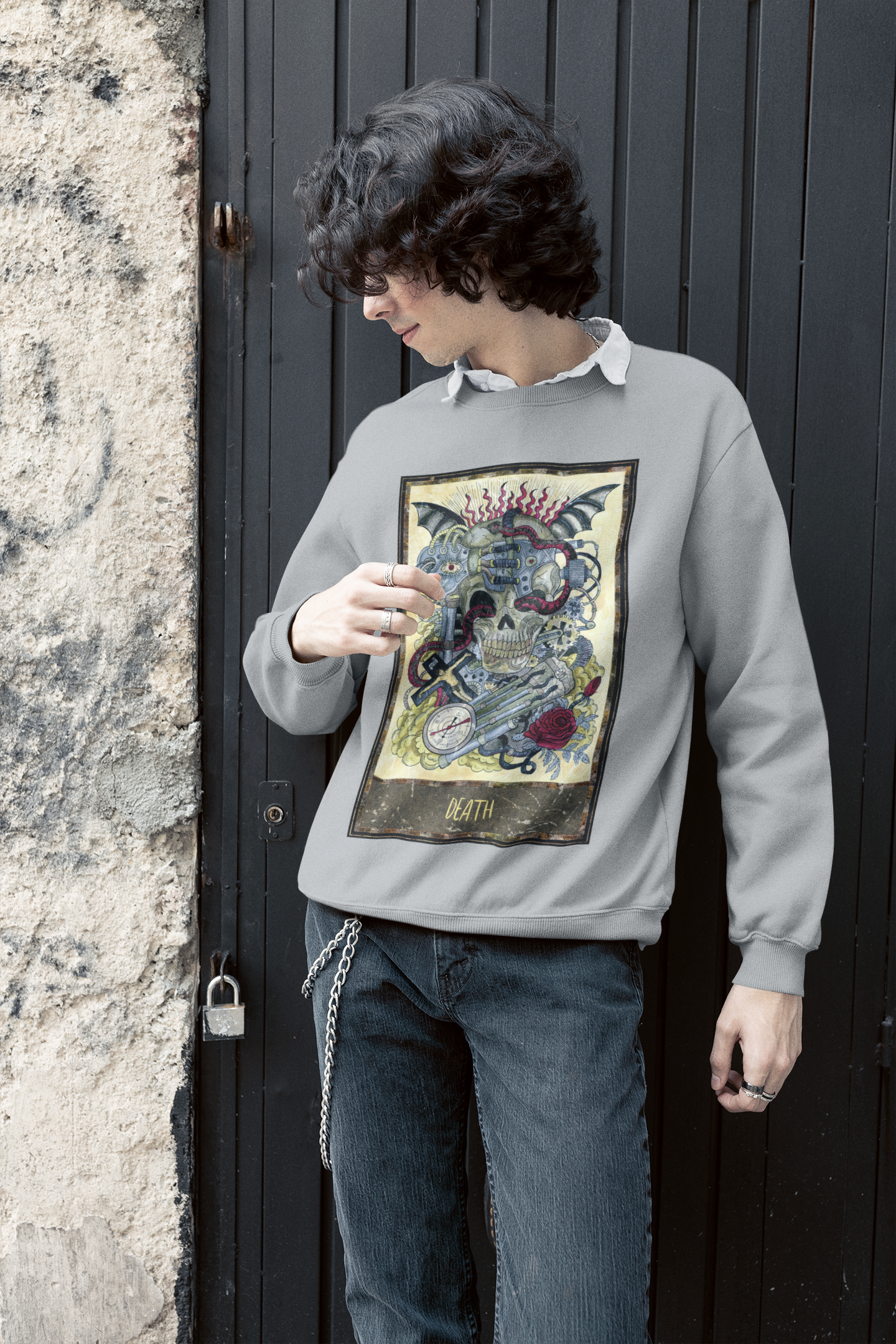 A boy with curly hair wearing a grey Death Tarot Card Sweatshirt over a white collar shirt, and dark blue jeans with chains