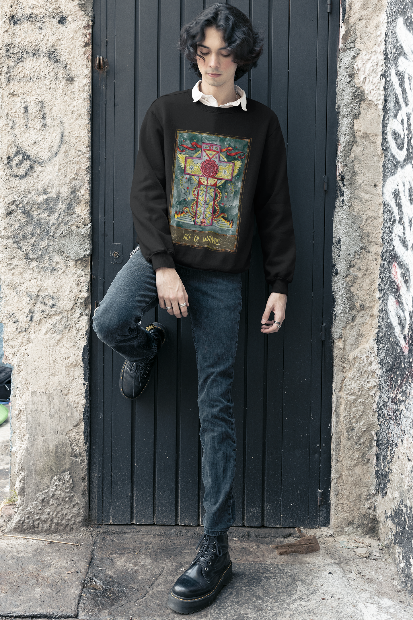 A young boy wearing a black Ace of Wands Tarot Card Sweatshirt outside of a white collar shirt, dark blue jeans, and black boots