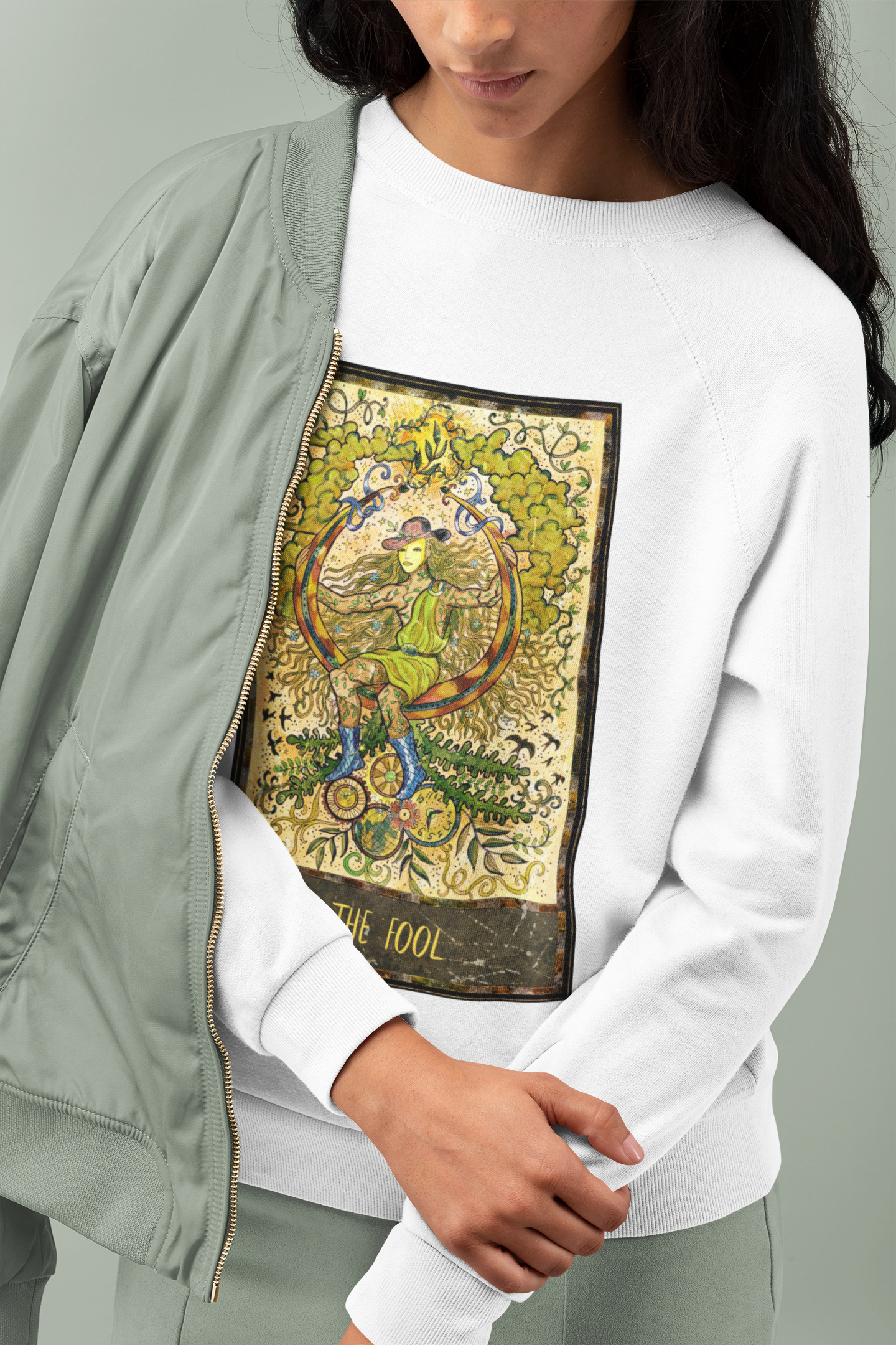 A woman with long hair wearing a white The Fool Tarot Card Sweatshirt and green pastel bomber jacket and pants