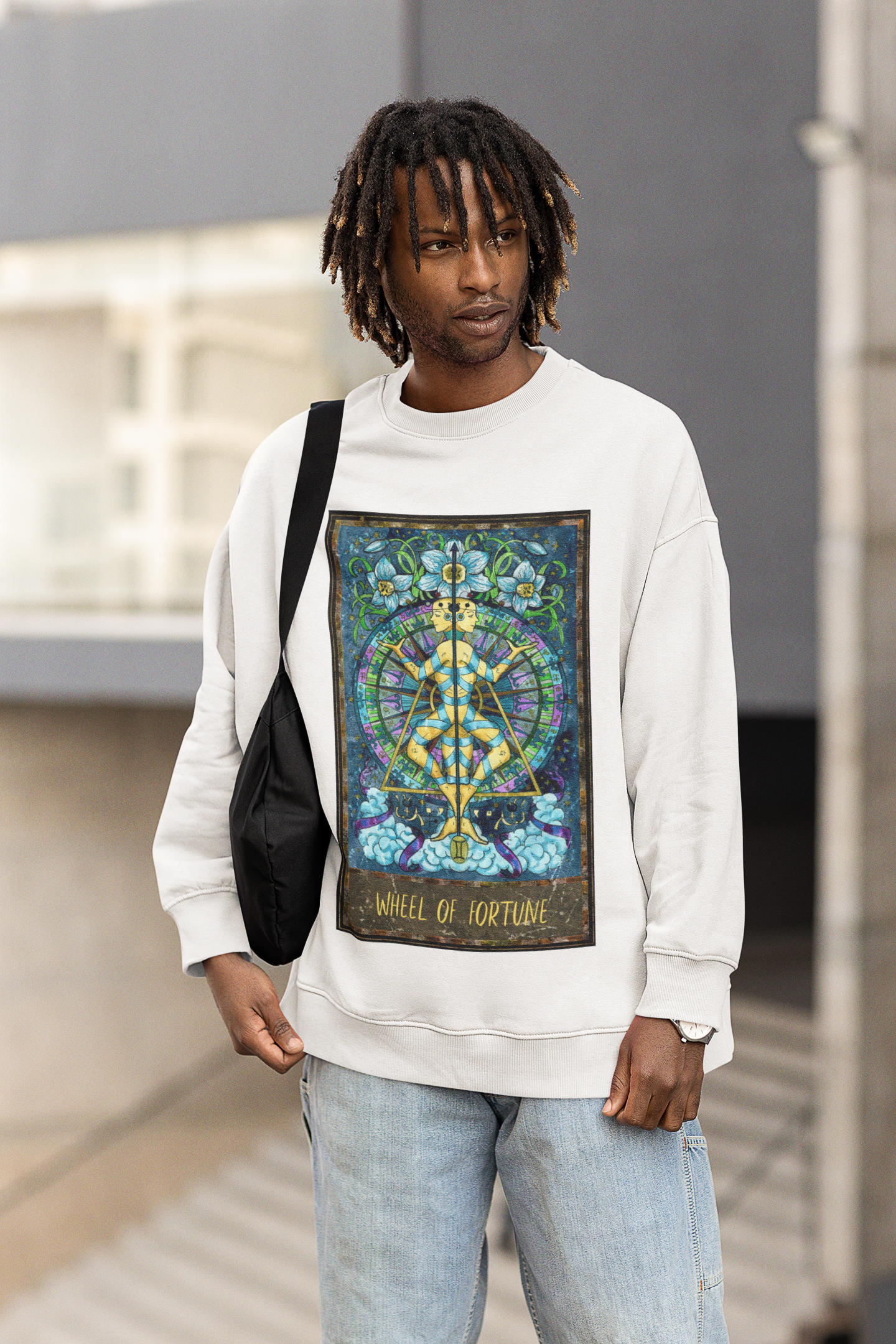 A man carrying a bag wearing a white Wheel of Fortune Tarot Card Sweatshirt and jeans