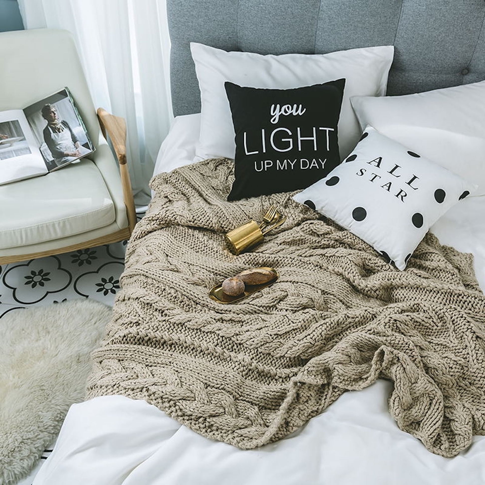 Khaki knitted throw blanket on a bed with pillows and other objects