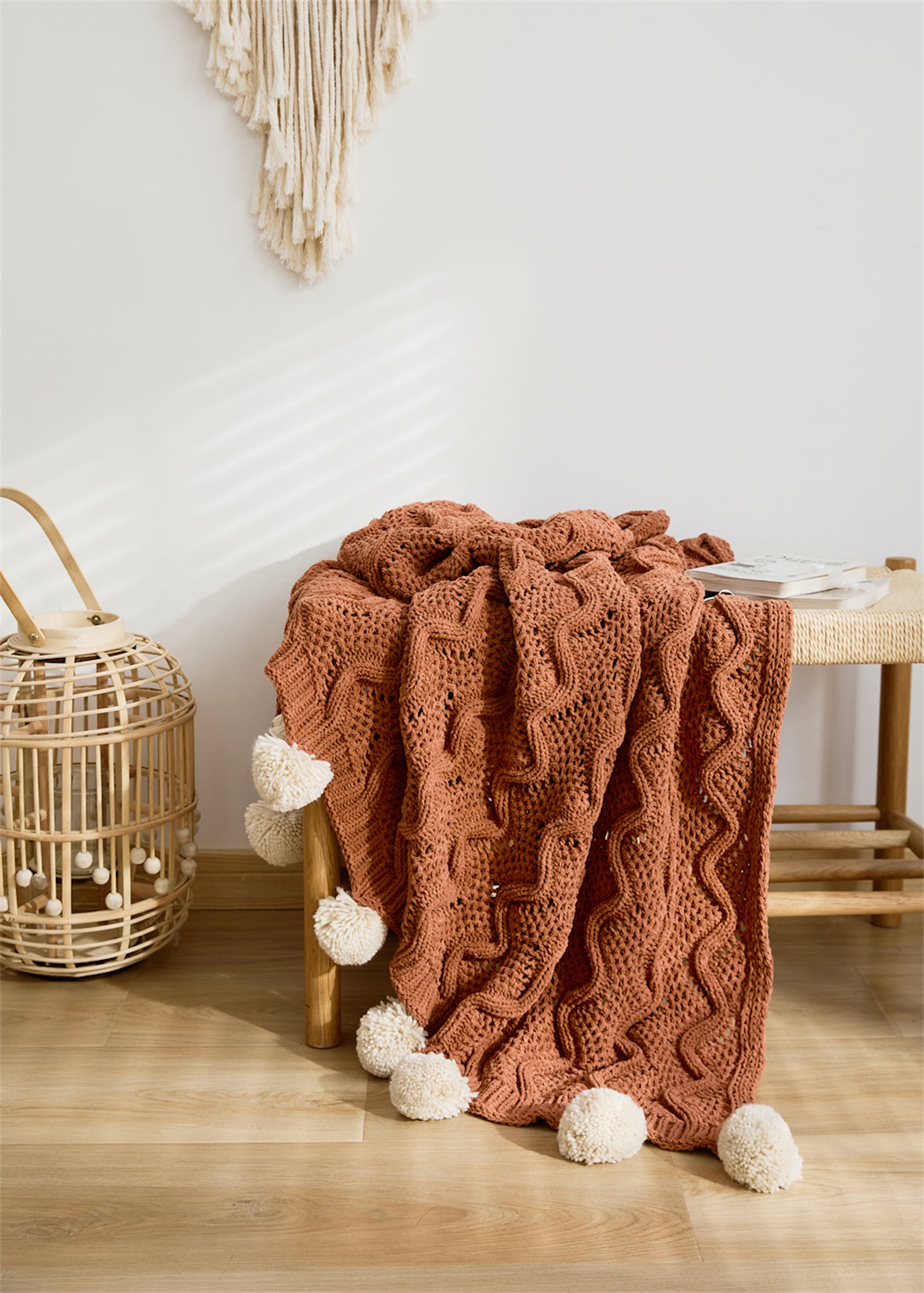 Rusty Orange Pompom Fringes Solid Chenille Knitted Throw Blanket draping on a short shelf