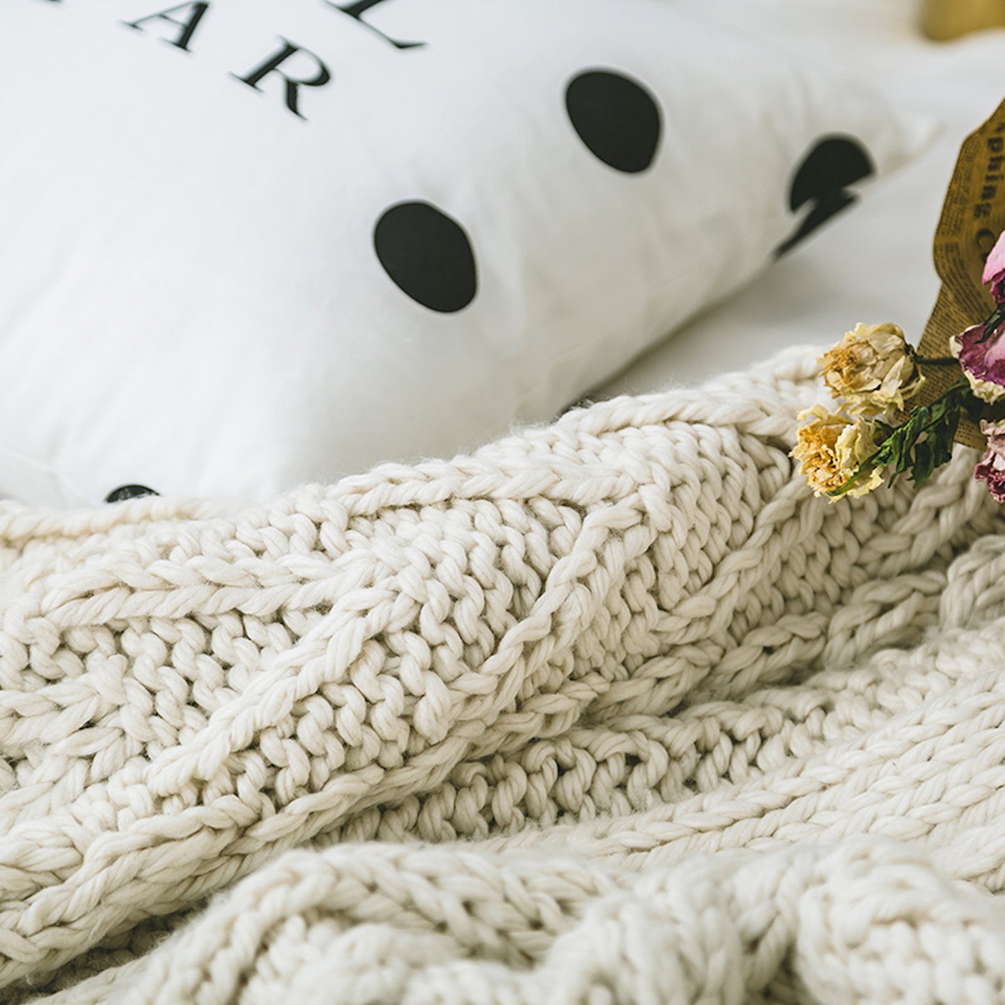 close up shot of a beige knitted throw blanket next to a polka dotted pillow