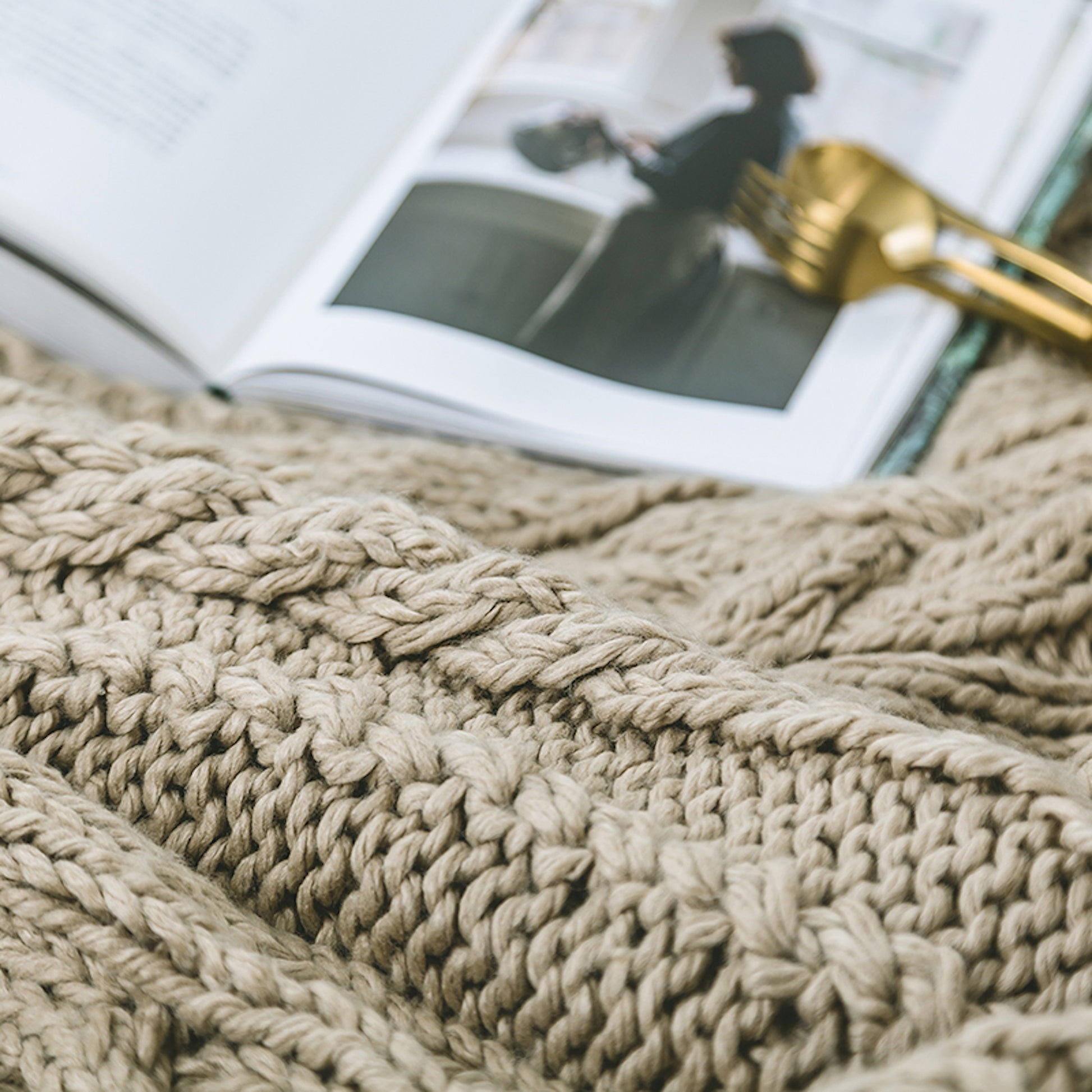 close up shot of a khaki knitted throw blanket next to a book