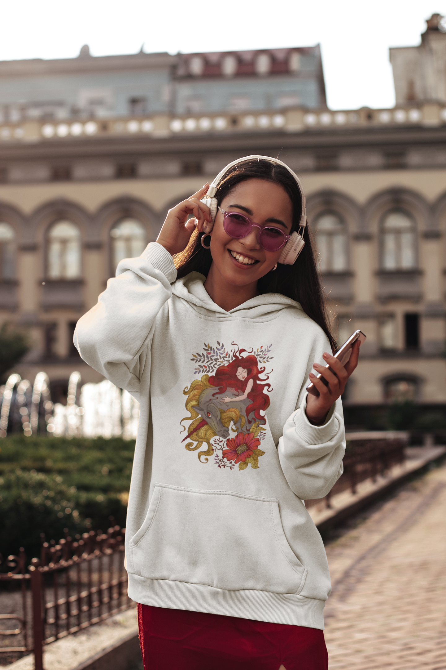 A woman with headphones and sunglasses wearing a white Red Princess and Magic Unicorn Hoodie and red skirt