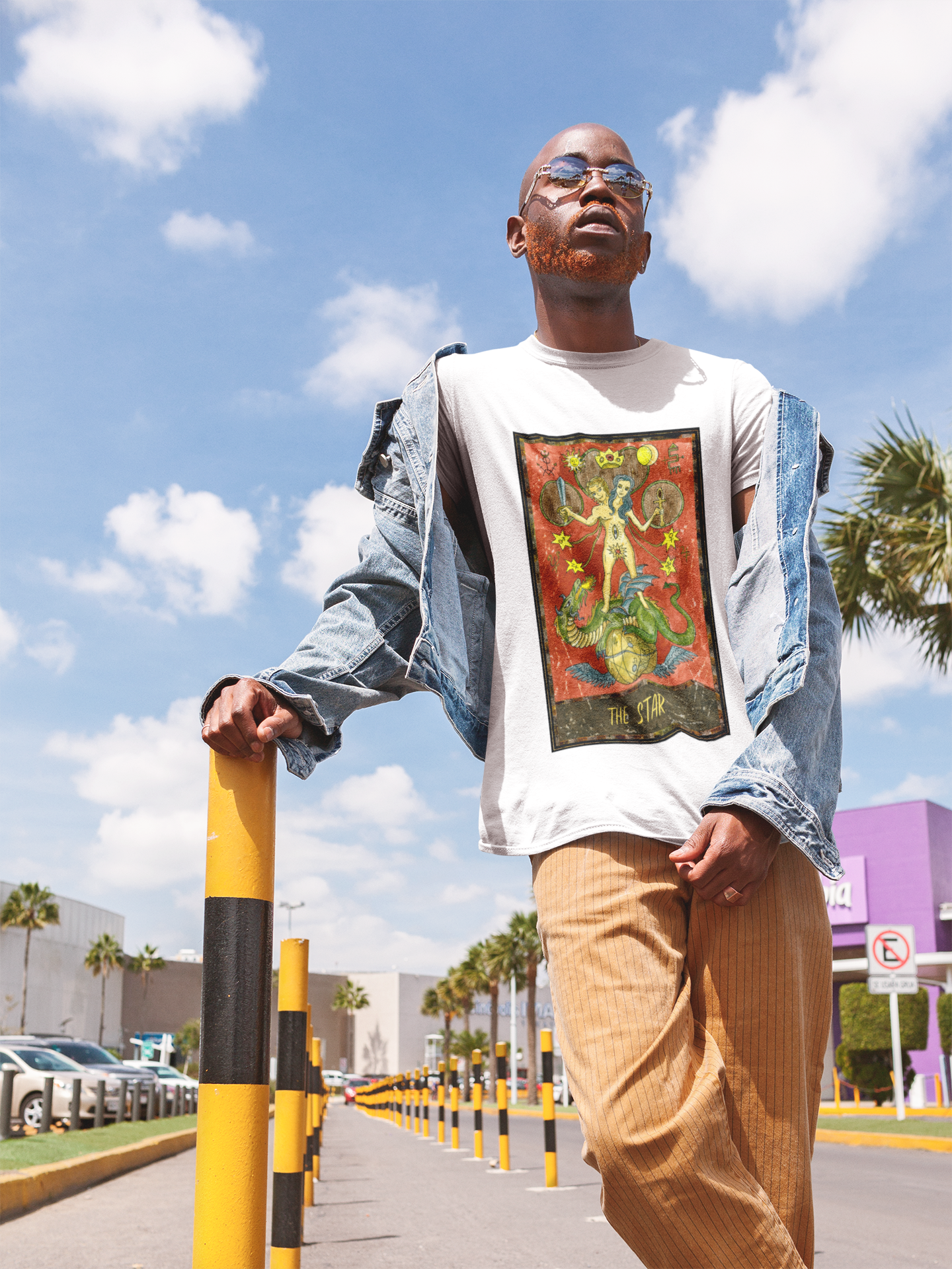 A man with sunglasses wearing a white The Star Tarot Card T-Shirt, a denim jacket, an orange pant posing next to the pole