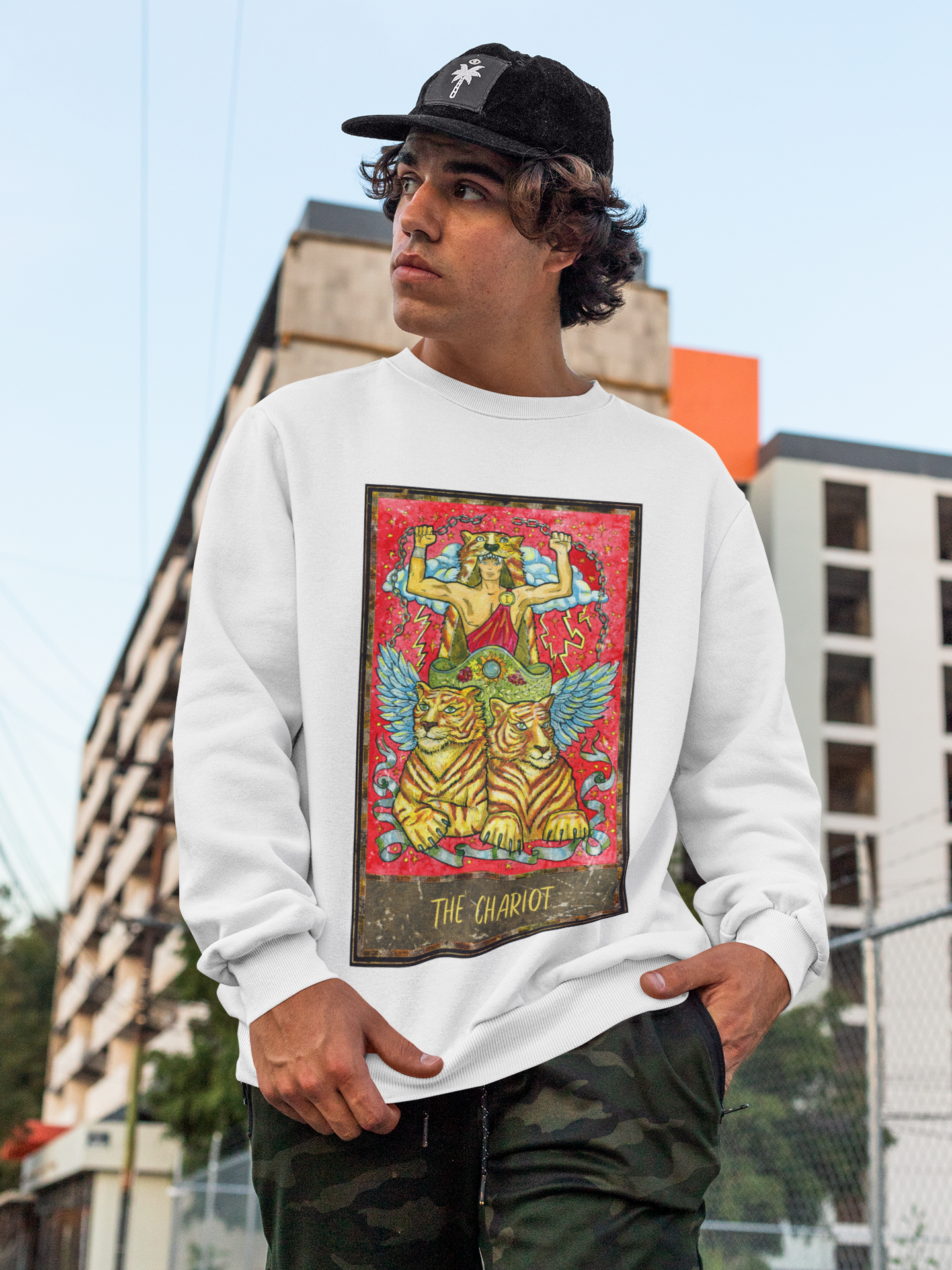 A man wearing a white The Chariot Tarot Card Sweatshirt and camo pants