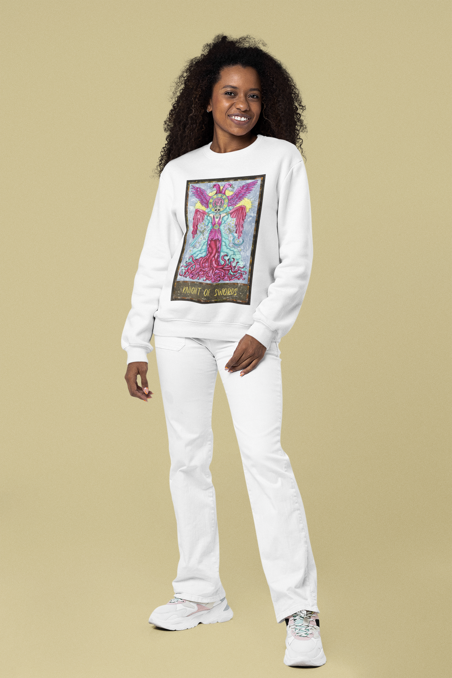 A curly haired woman wearing a white Knight of Swords Tarot Card Sweatshirt, white pants, and white shoes