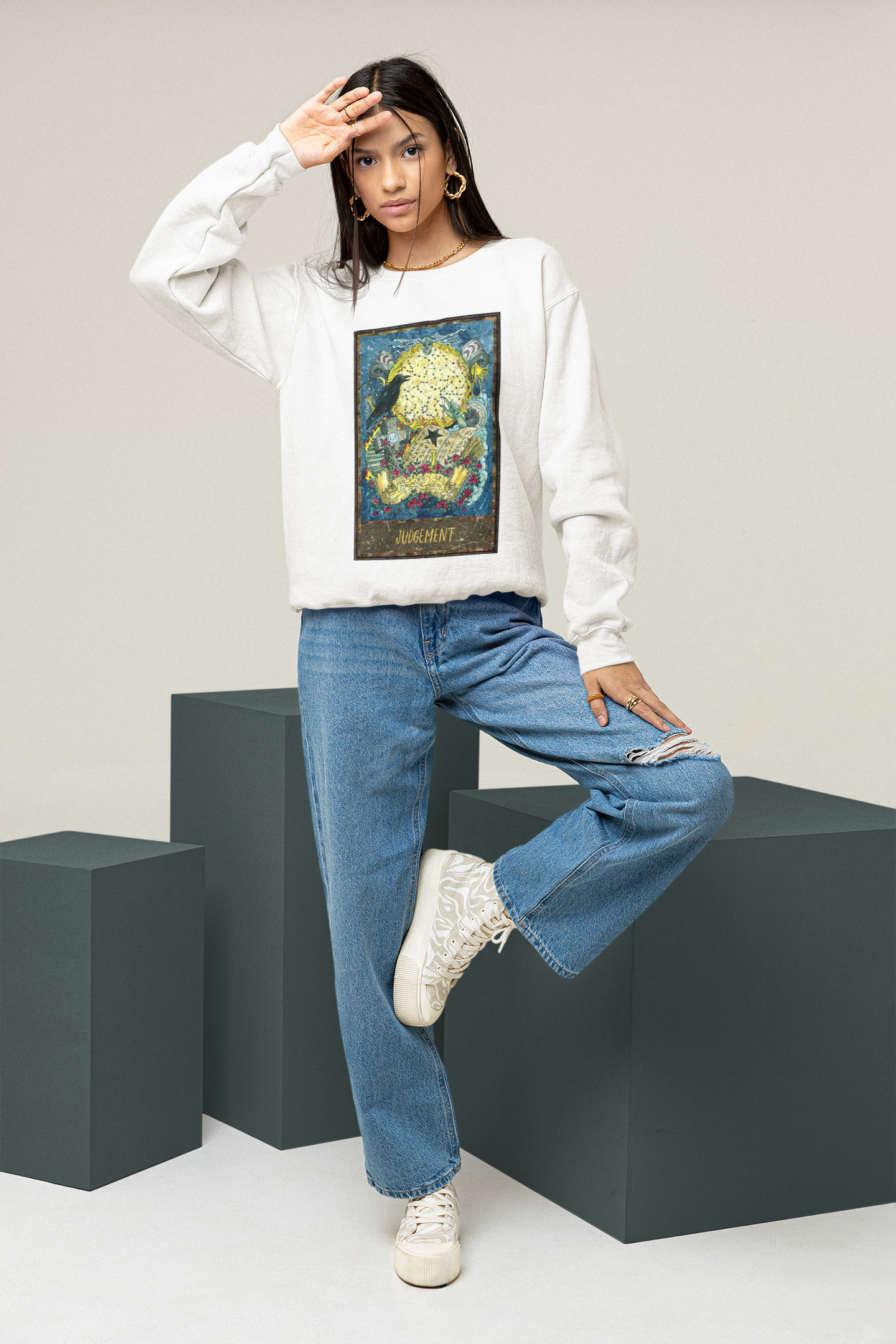 A woman posing in a studio wearing a white  Judgement - Tarot Card Sweatshirt, blue jeans, and white shoes