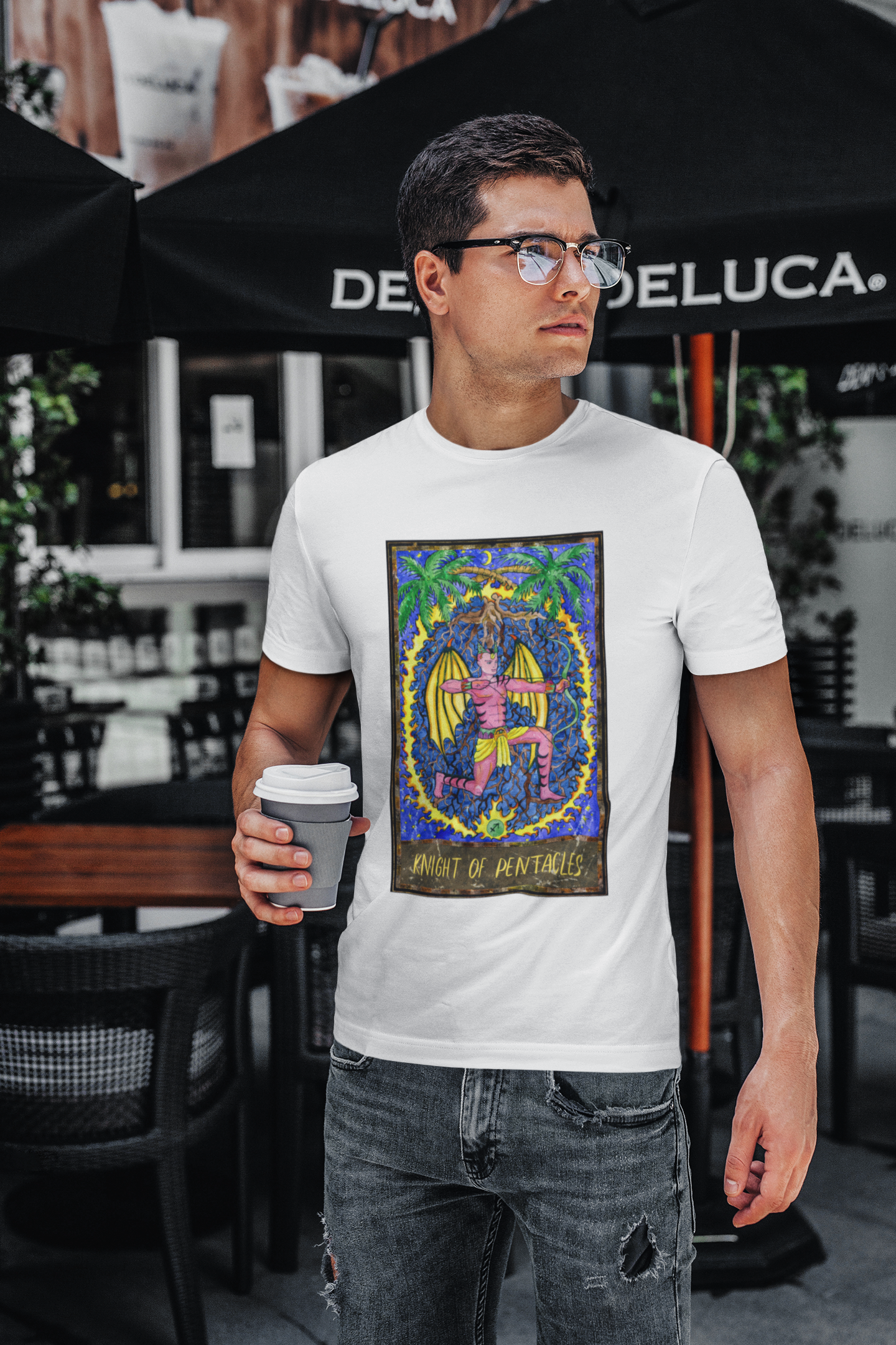 A man with glasses holding a coffee cup, wearing a white Knight of Pentacles Tarot Card T-shirt and ripped jeans