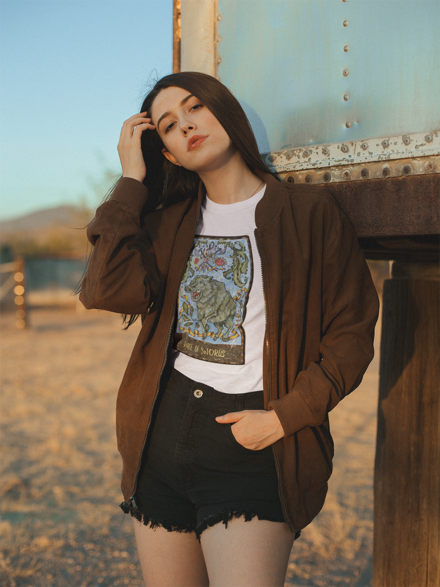 A woman wearing a white Page of Swords Tarot Card T-shirt, a brown jacket and black shorts