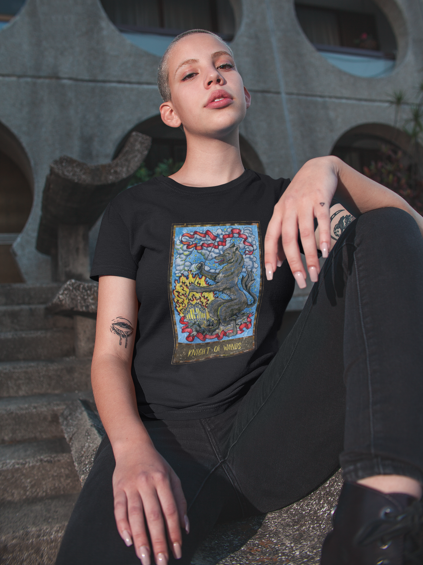 A woman with a buzz cut haircut wearing a black Knight of Wands Tarot Card T-shirt, black pants, and black shoes