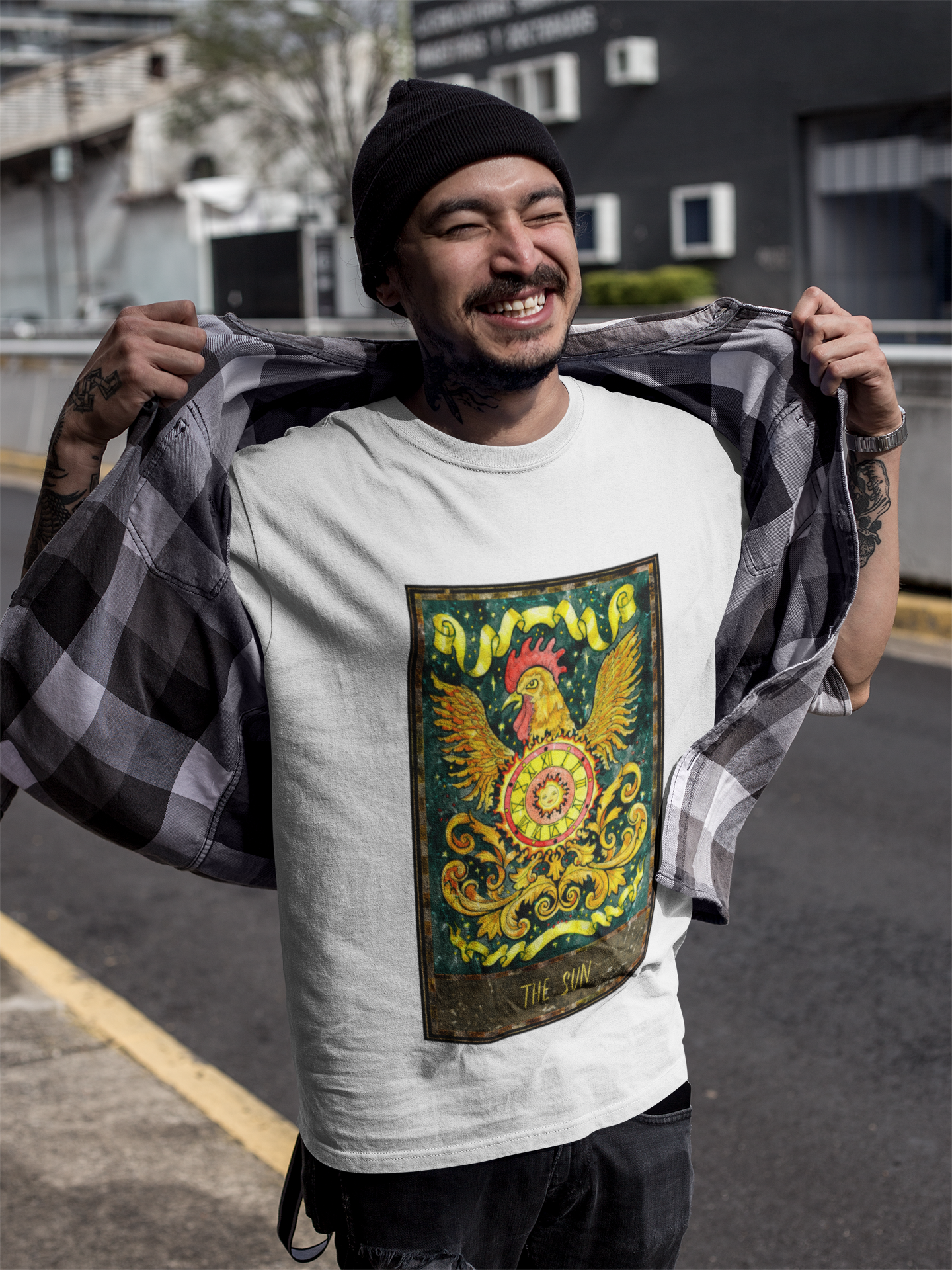 A smiling man wearing a black beanie, white The Sun Tarot Card T-Shirt, a collar shirt, and black pants 