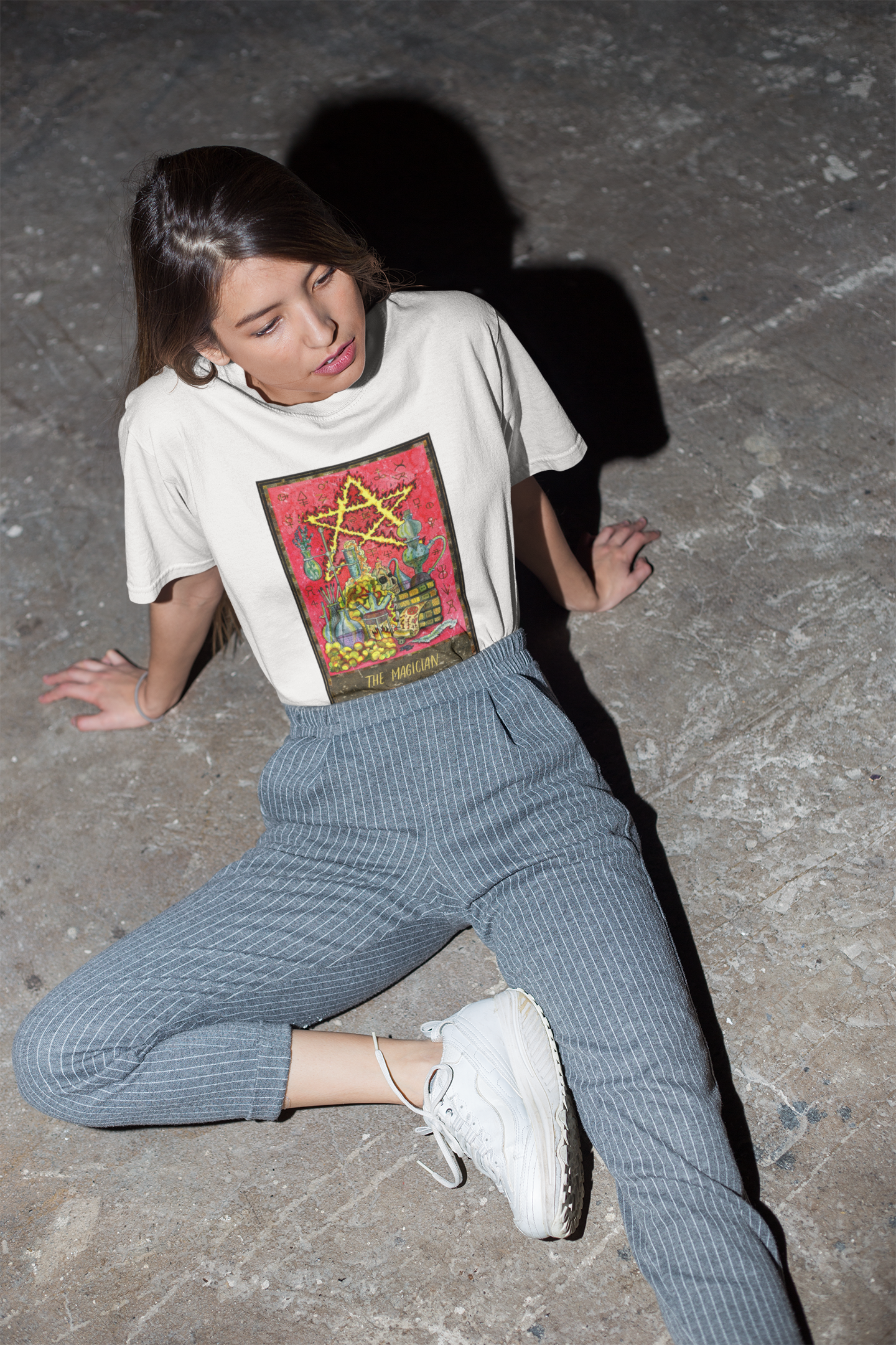 A woman posing on the ground wearing a white The Magician Tarot Card T-shirt, stripe pants and white shoes